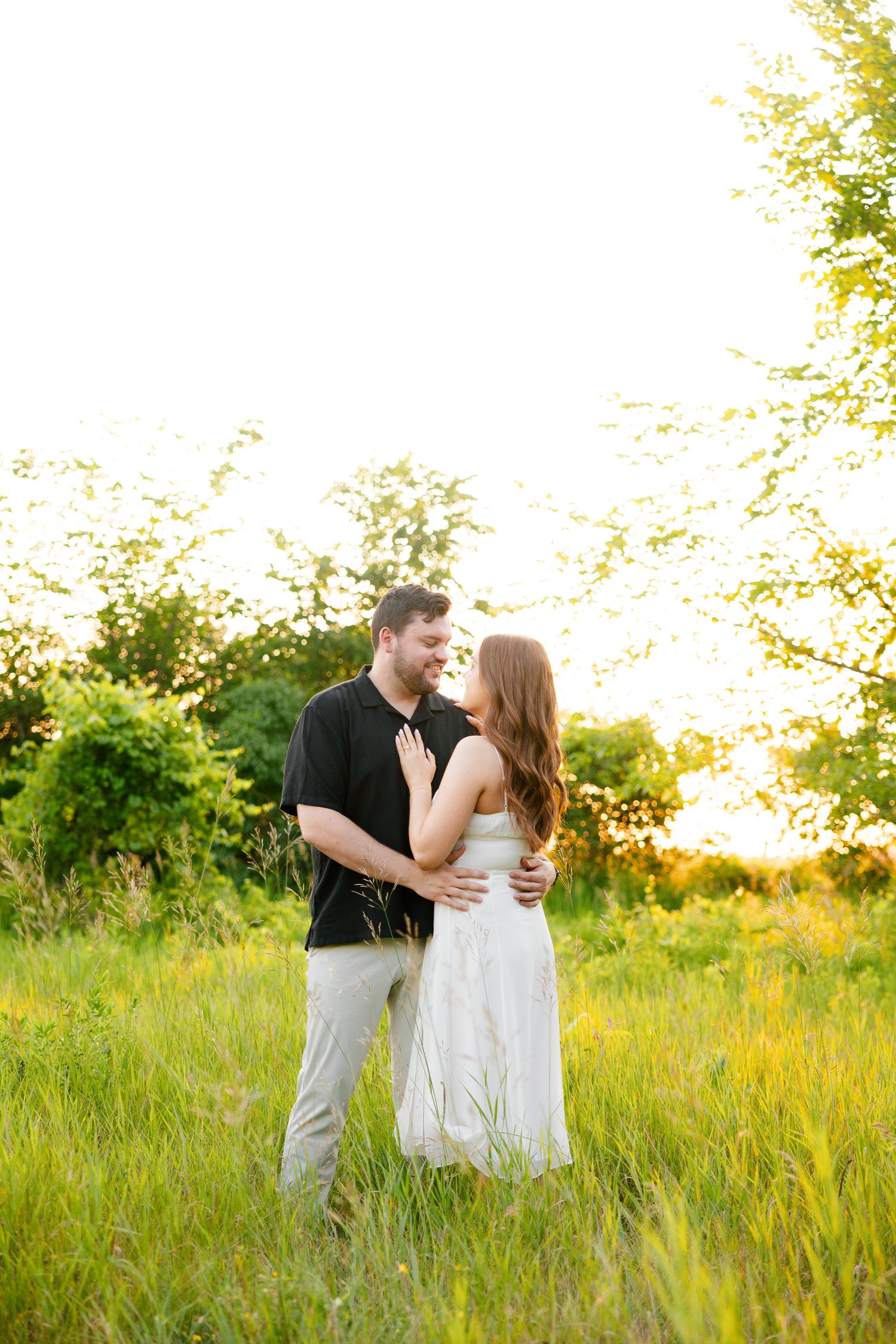 Loving couple embraces in tall grass field during golden hour photography session.