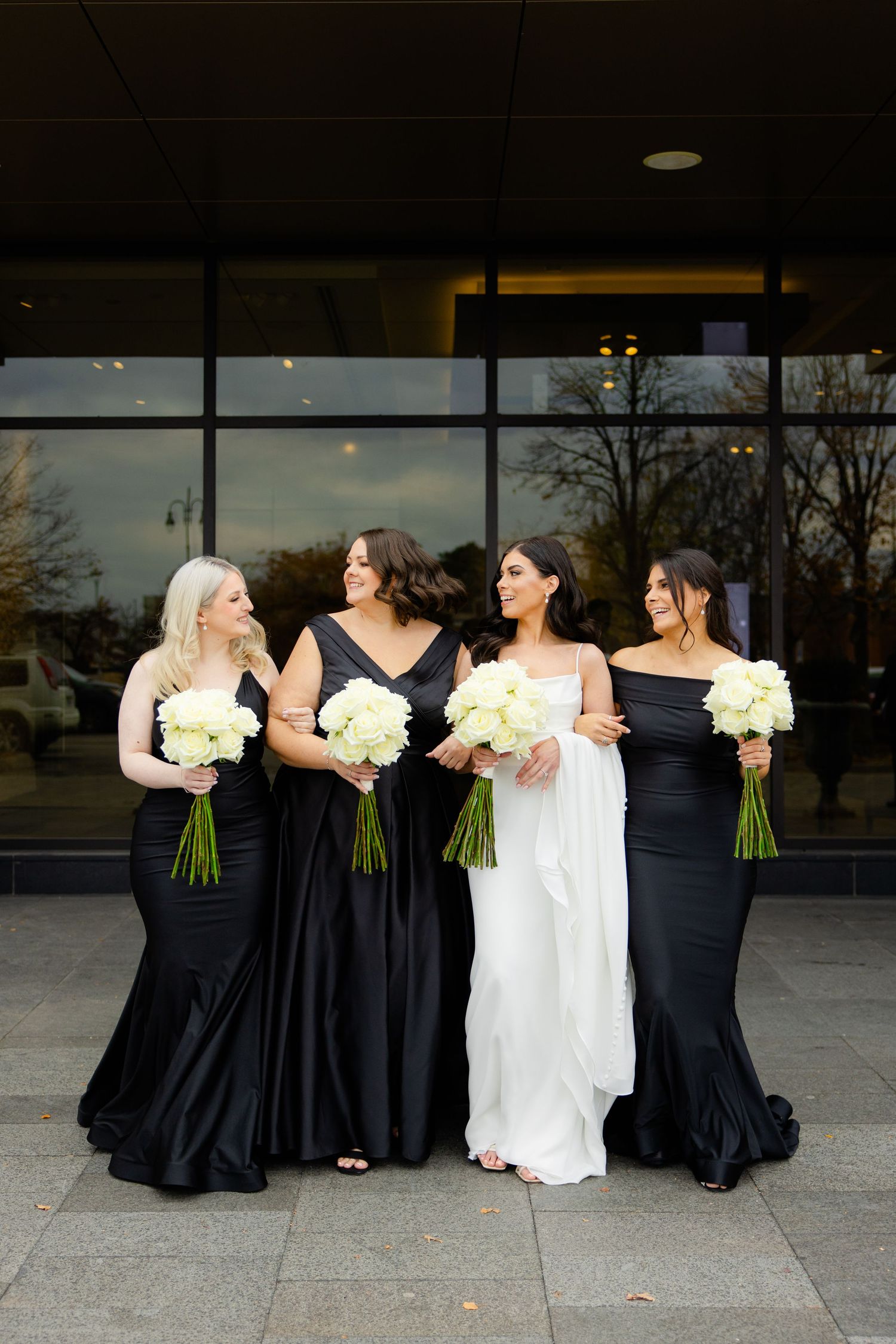 Wedding party photo featuring bridesmaids in elegant black dresses with white bouquets alongside bride in white.