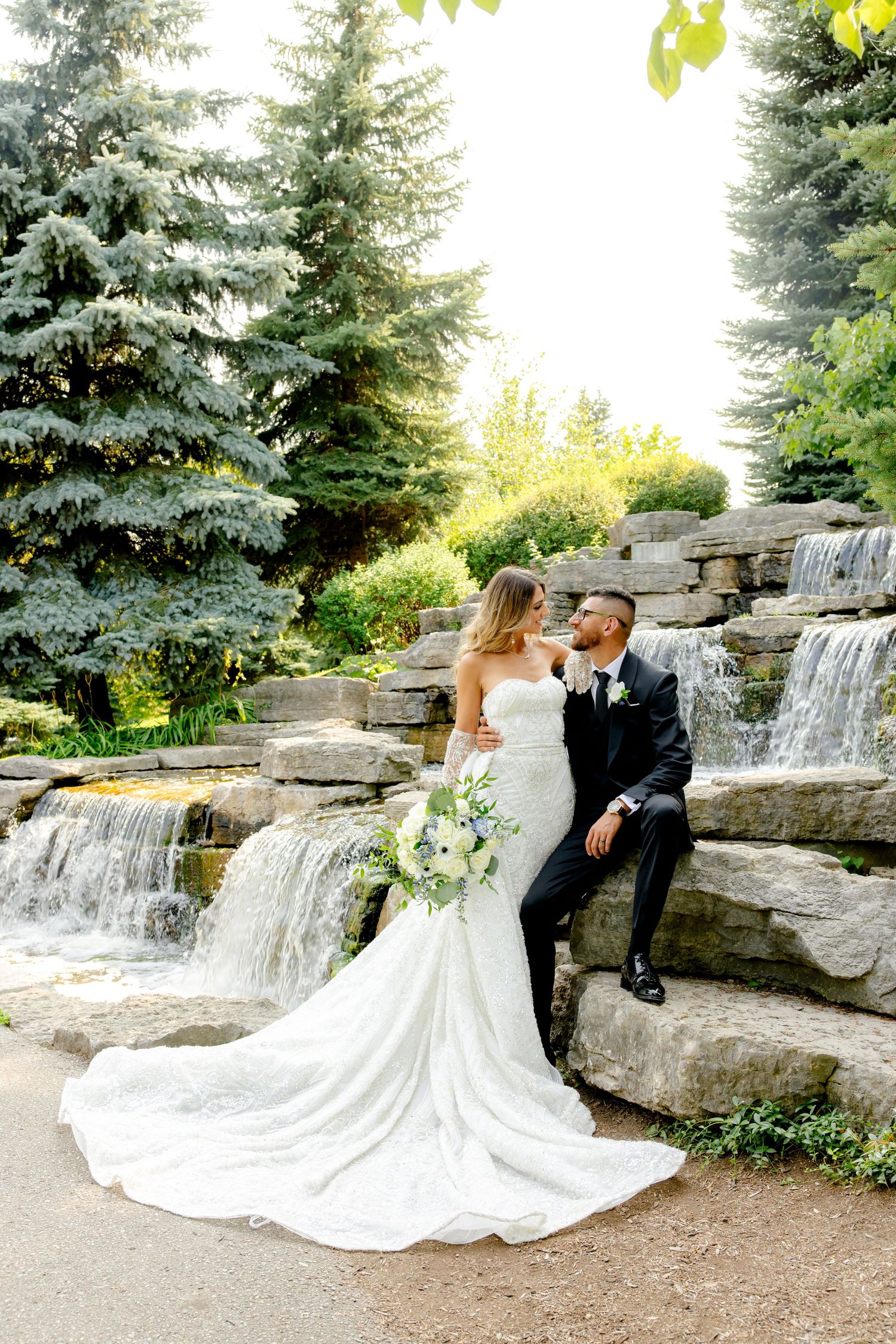 Wedding couple shares intimate moment on stone waterfall steps with flowing water and evergreens.