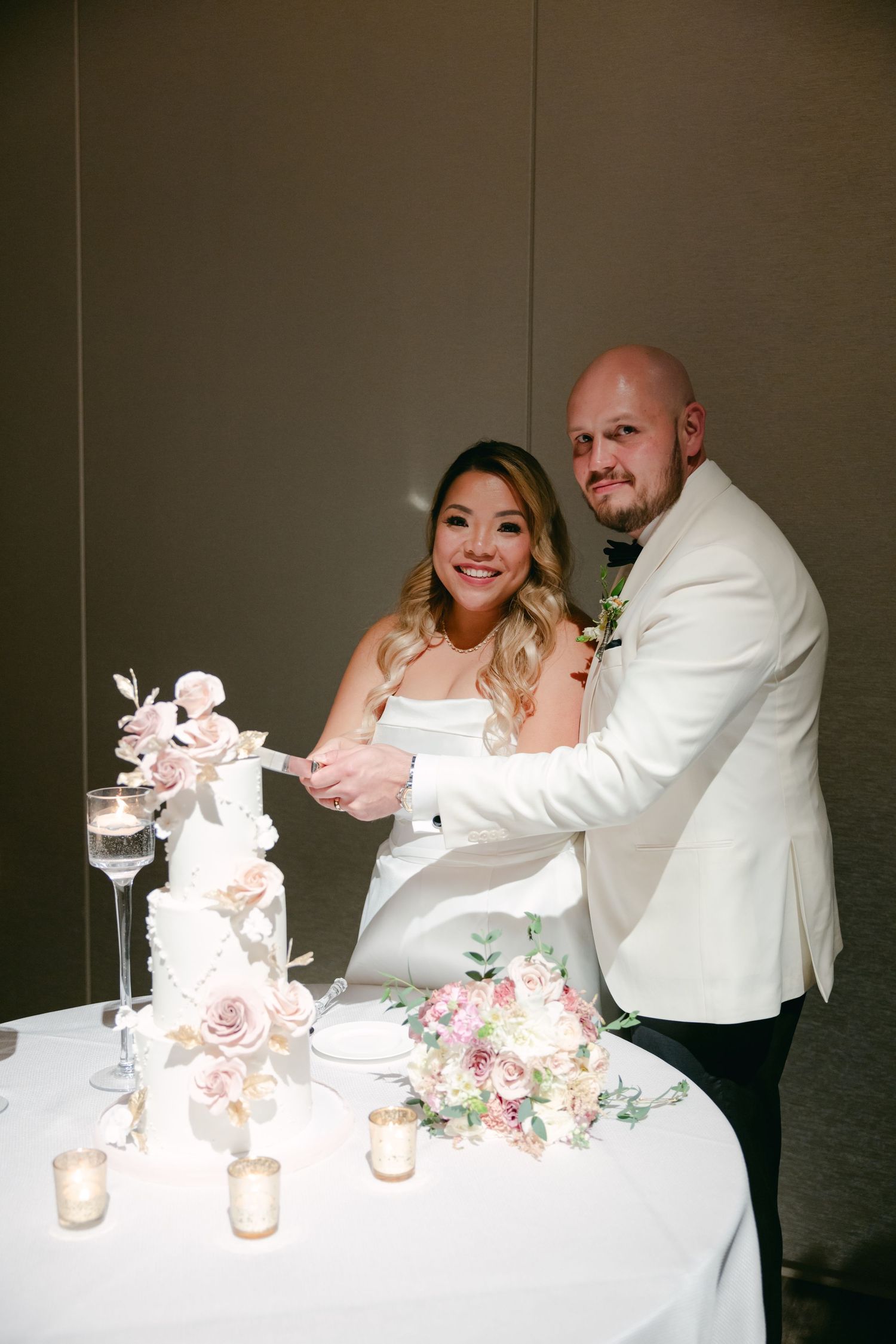 Newlyweds cut their elegant white wedding cake decorated with pink roses.