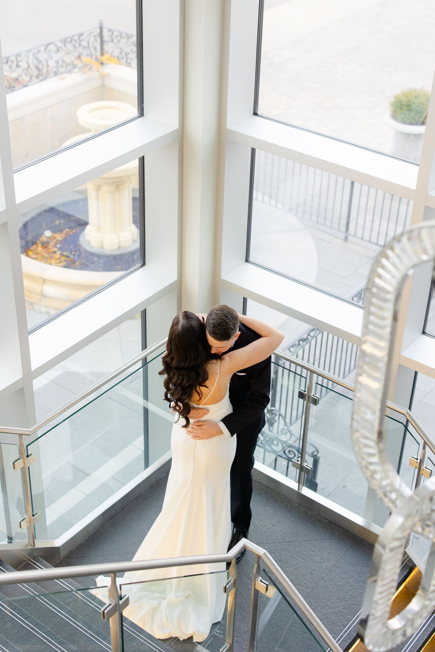 Overhead view of wedding couple dancing in formal attire near large windows and modern architectural details.