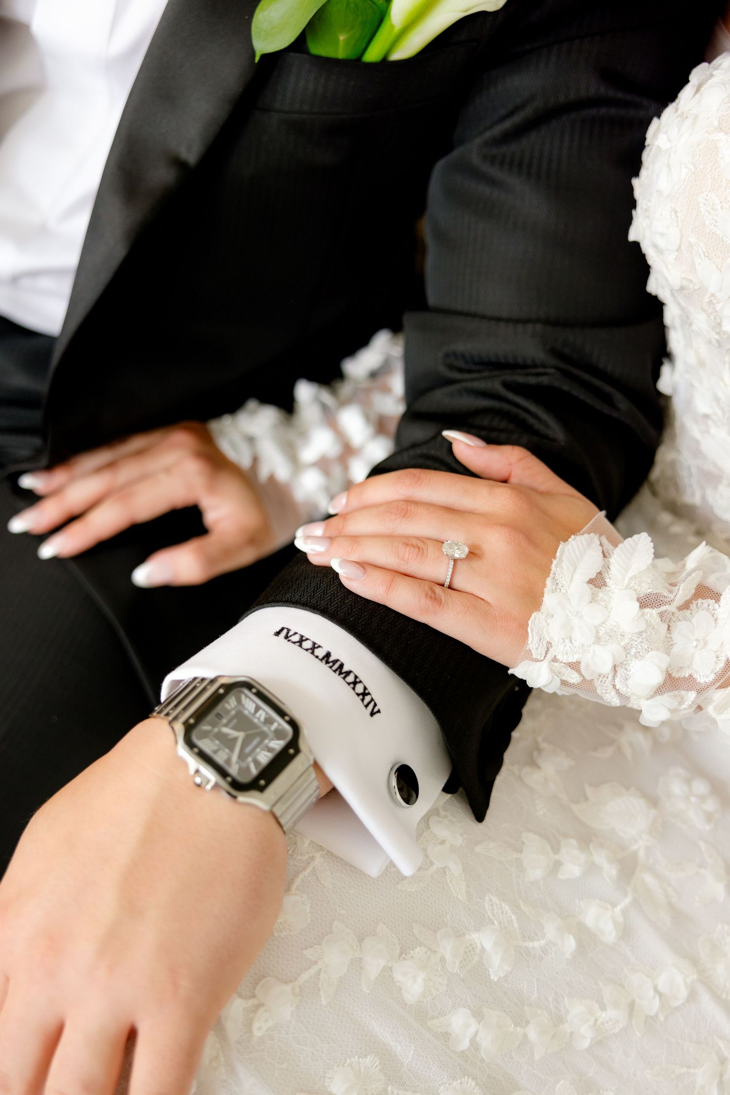 Close-up detail of hands showing a wedding ring and watch against formal wedding attire.