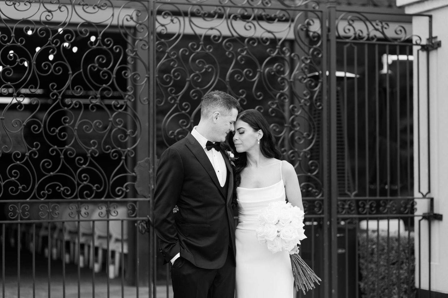Intimate black and white portrait of newlyweds against decorative iron gates.