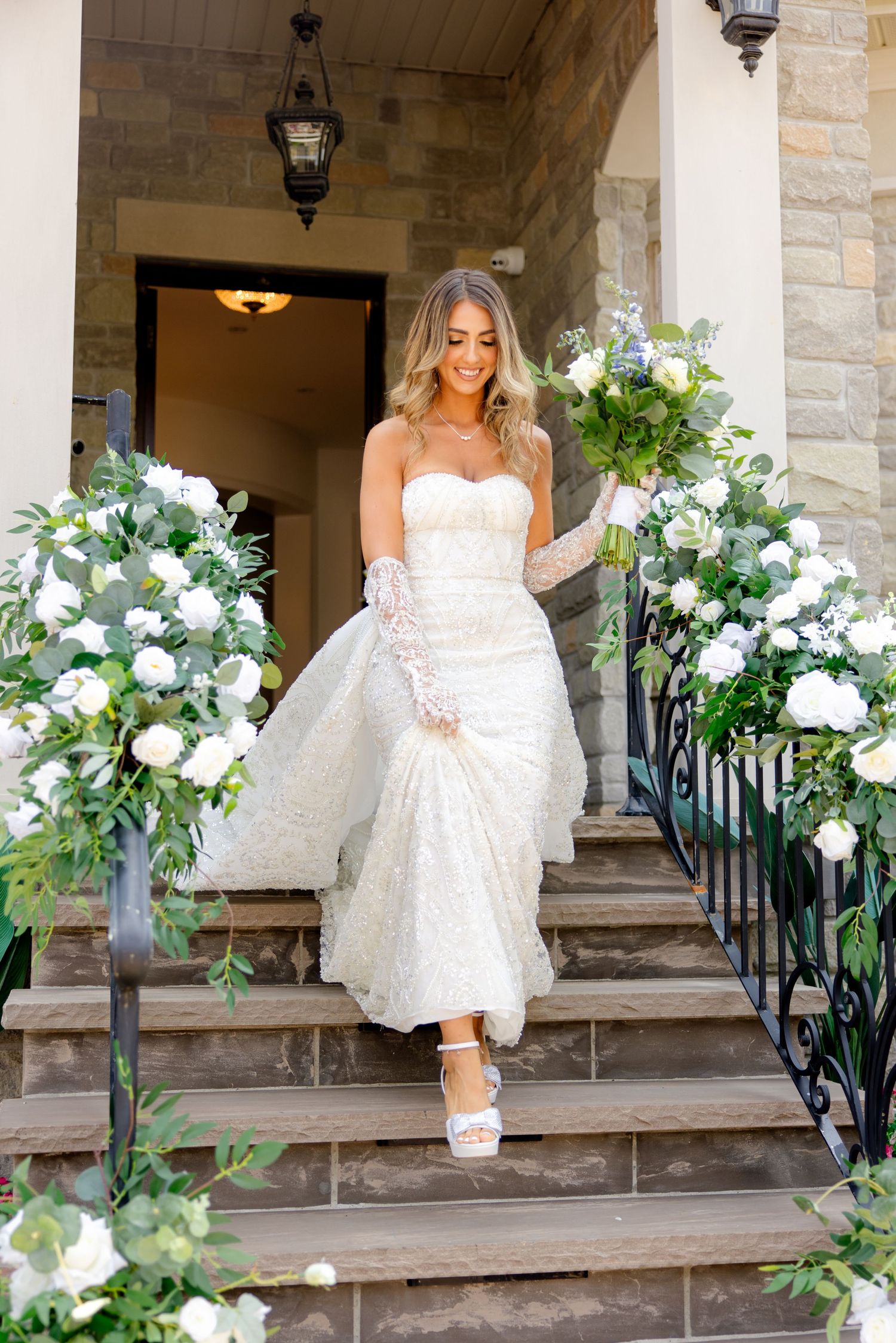 A bridal portrait on stone steps decorated with elegant white and blue floral arrangements.