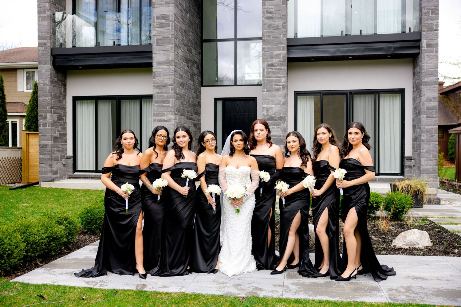 Wedding party with bridesmaids in elegant black gowns posing outside modern building.