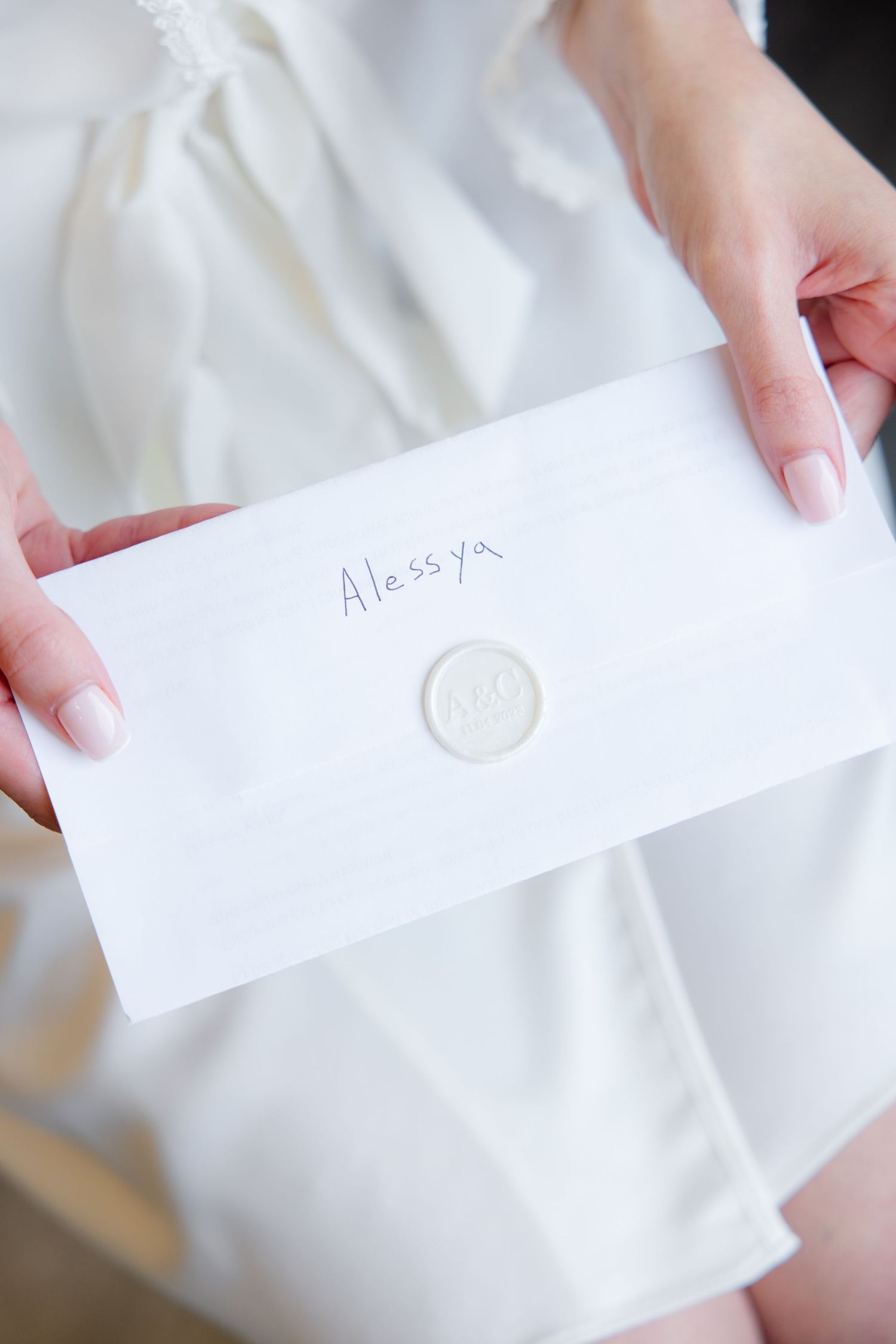 Hands holding white envelope with wax seal and handwritten text.