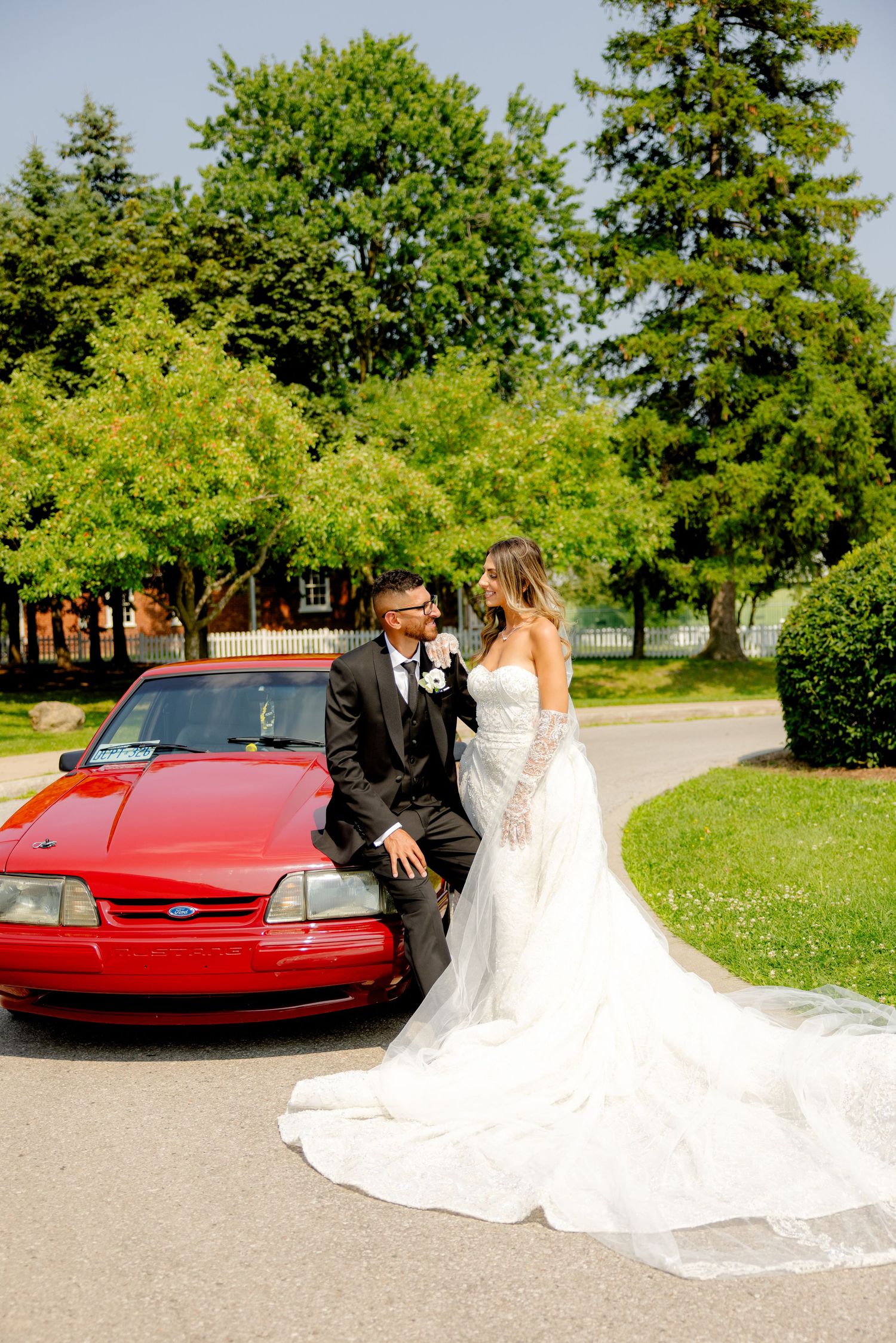 Elegant wedding portrait with a red car and beautiful landscaping in the background.