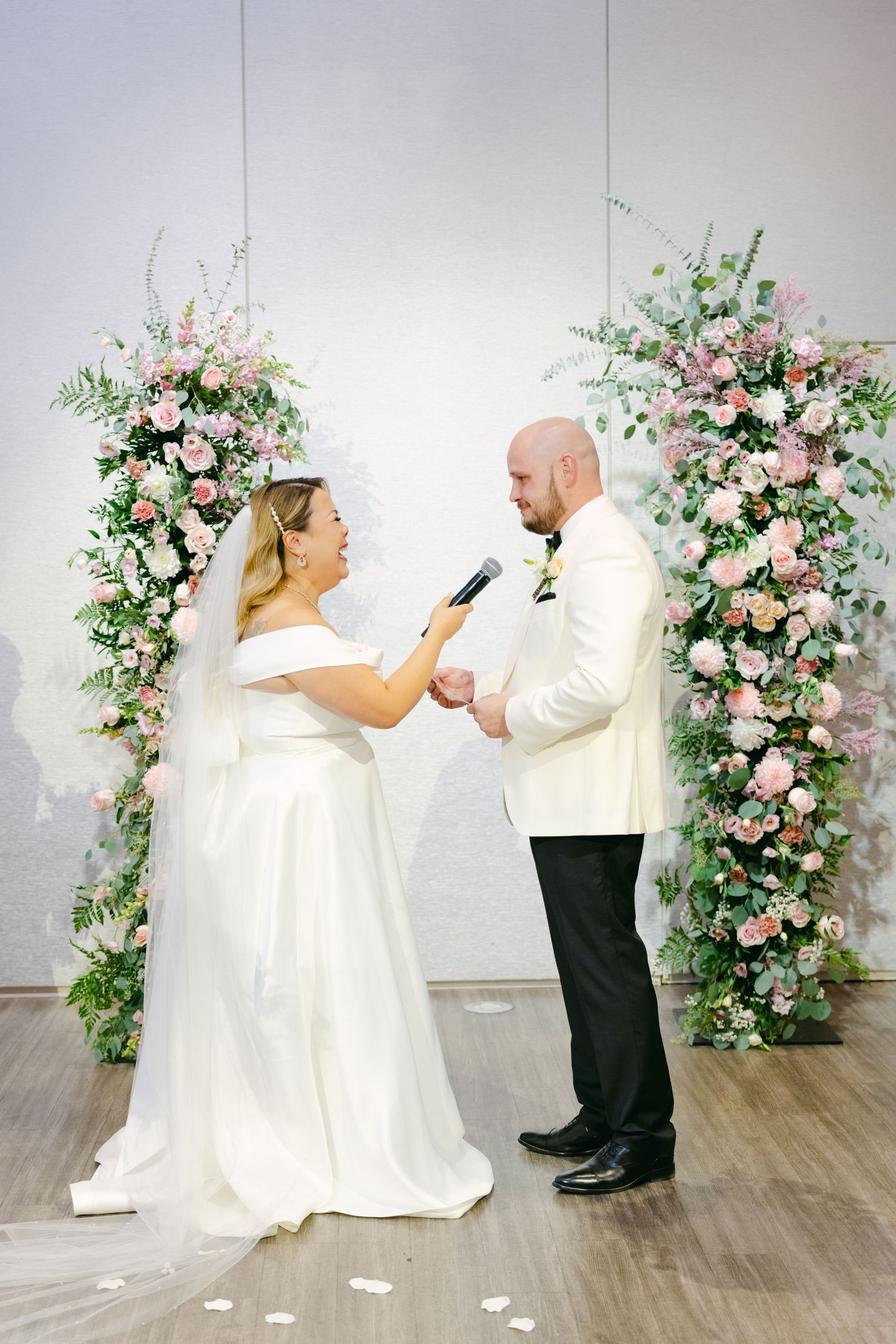 Couple sharing heartfelt moment under pink floral wedding arch during ceremony.