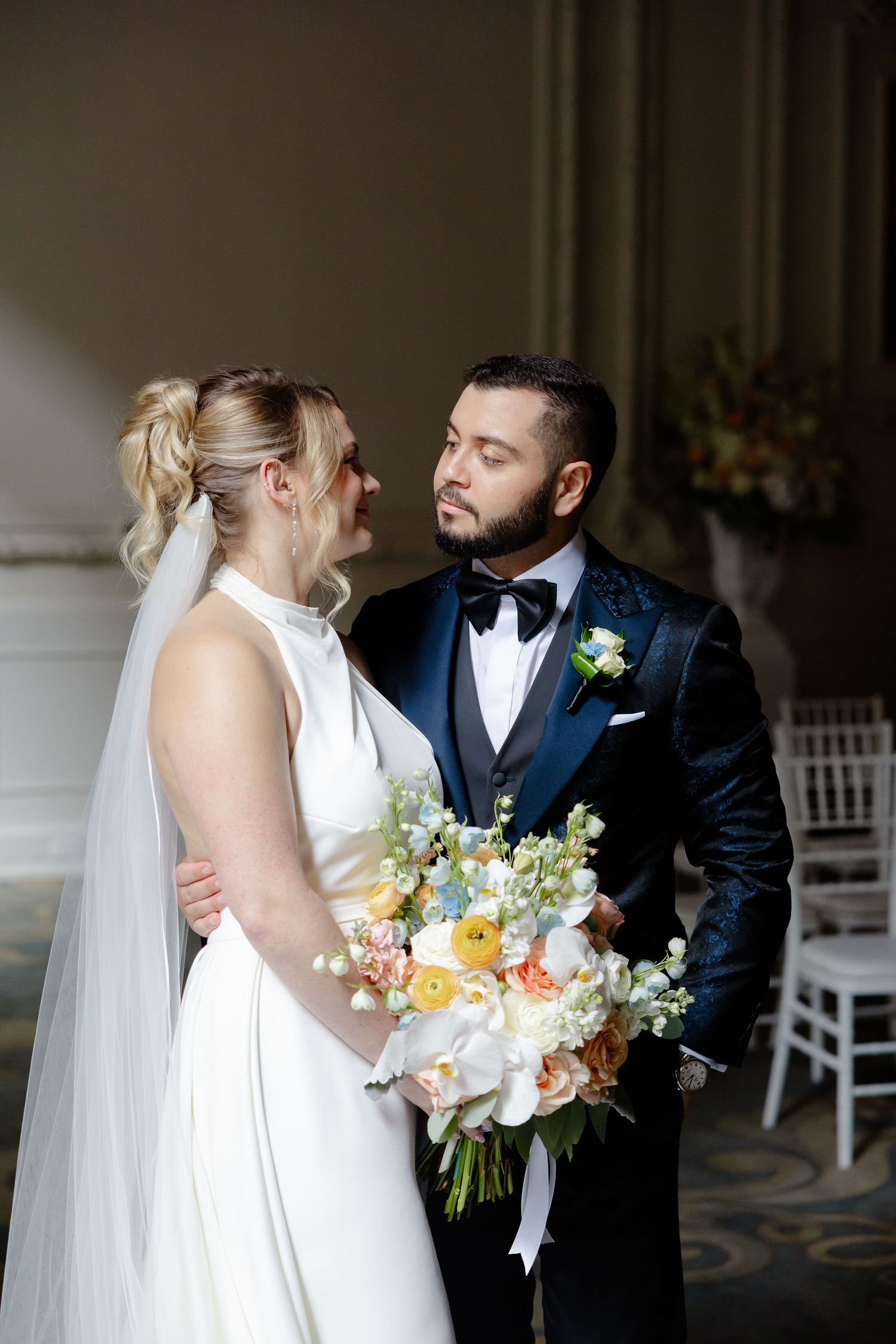 Wedding couple shares tender moment in formal attire against classic interior backdrop.