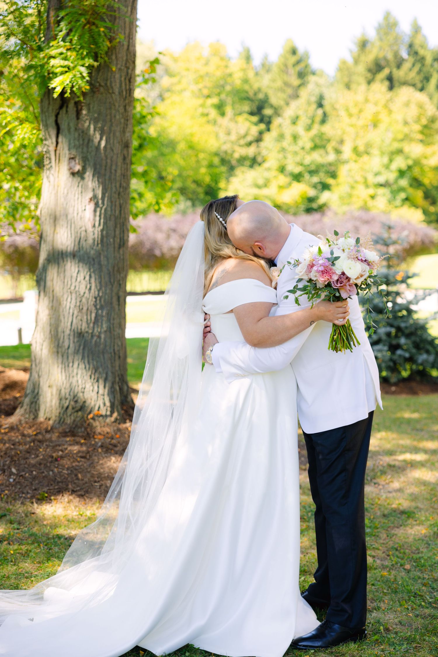 Romantic wedding moment captured in a sunlit garden with flowing white dress and floral bouquet.