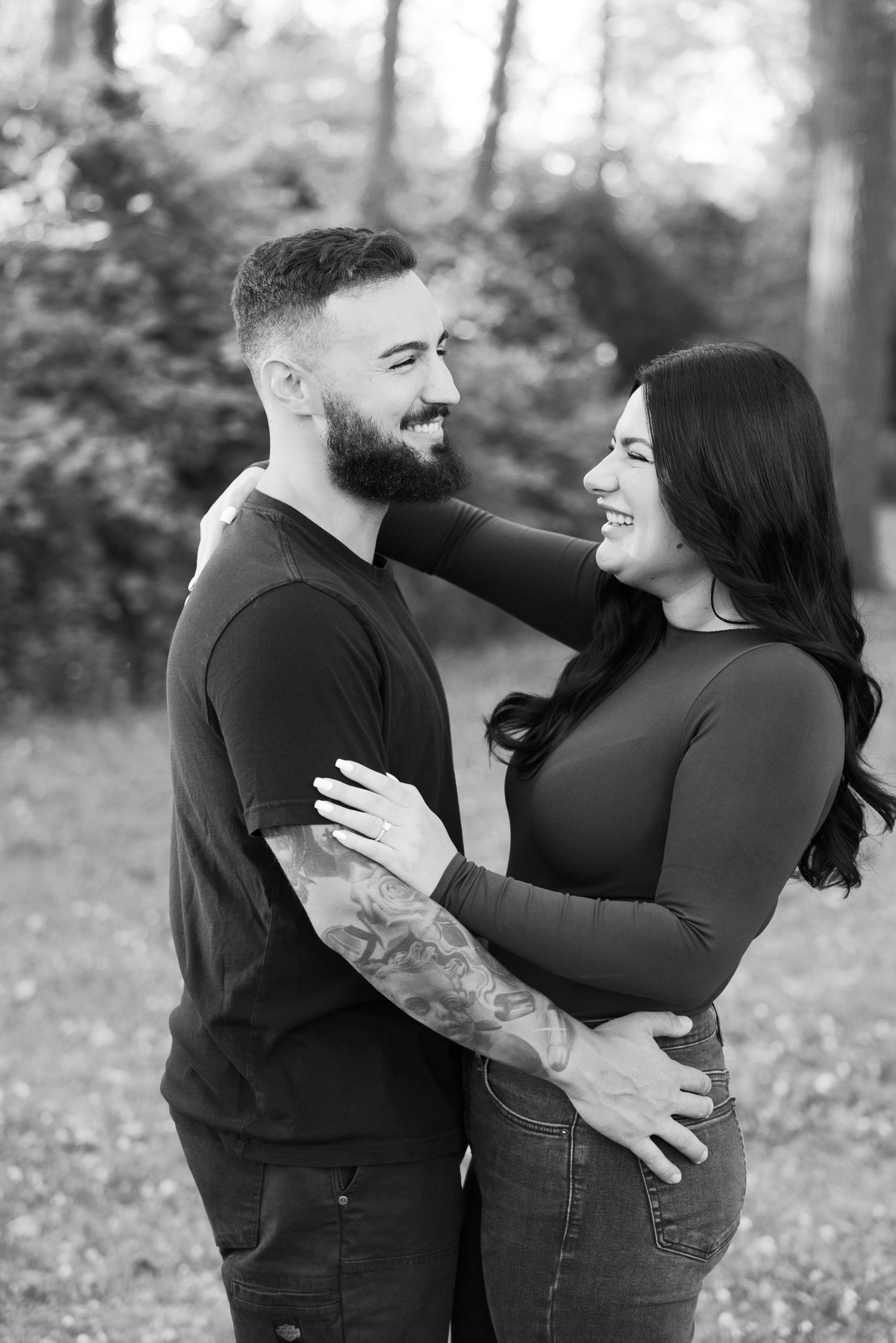 A black and white photo captures a couple sharing laughter during their outdoor photoshoot.