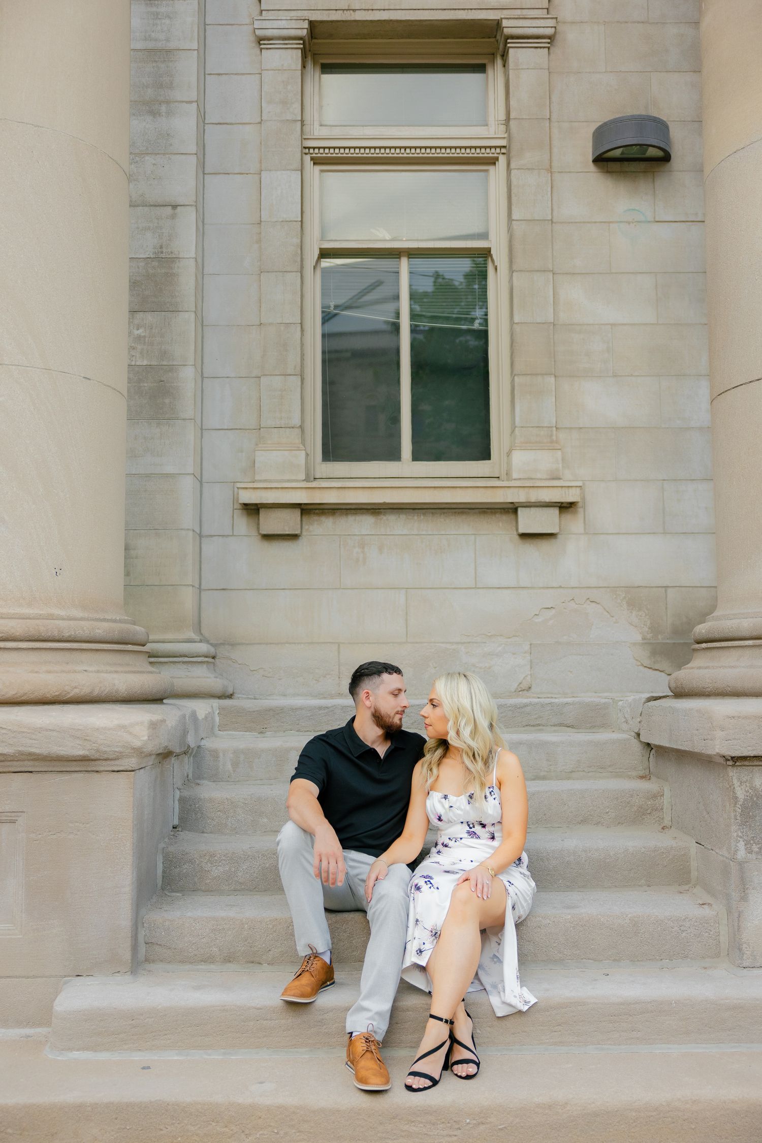 A couple sits romantically on stone steps of a historic building with elegant architecture.