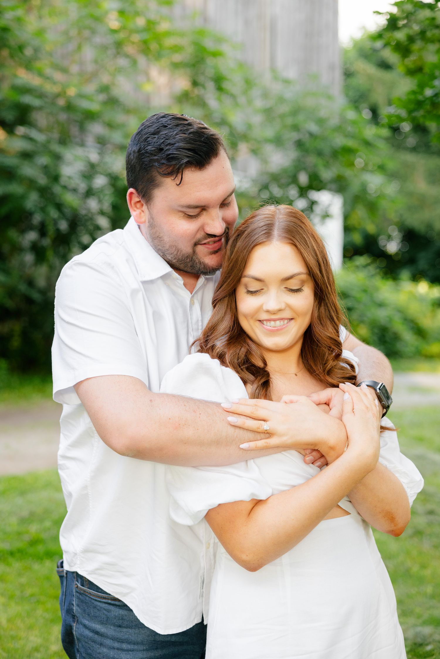 A tender moment between a couple wearing white as they embrace in a sunlit garden.