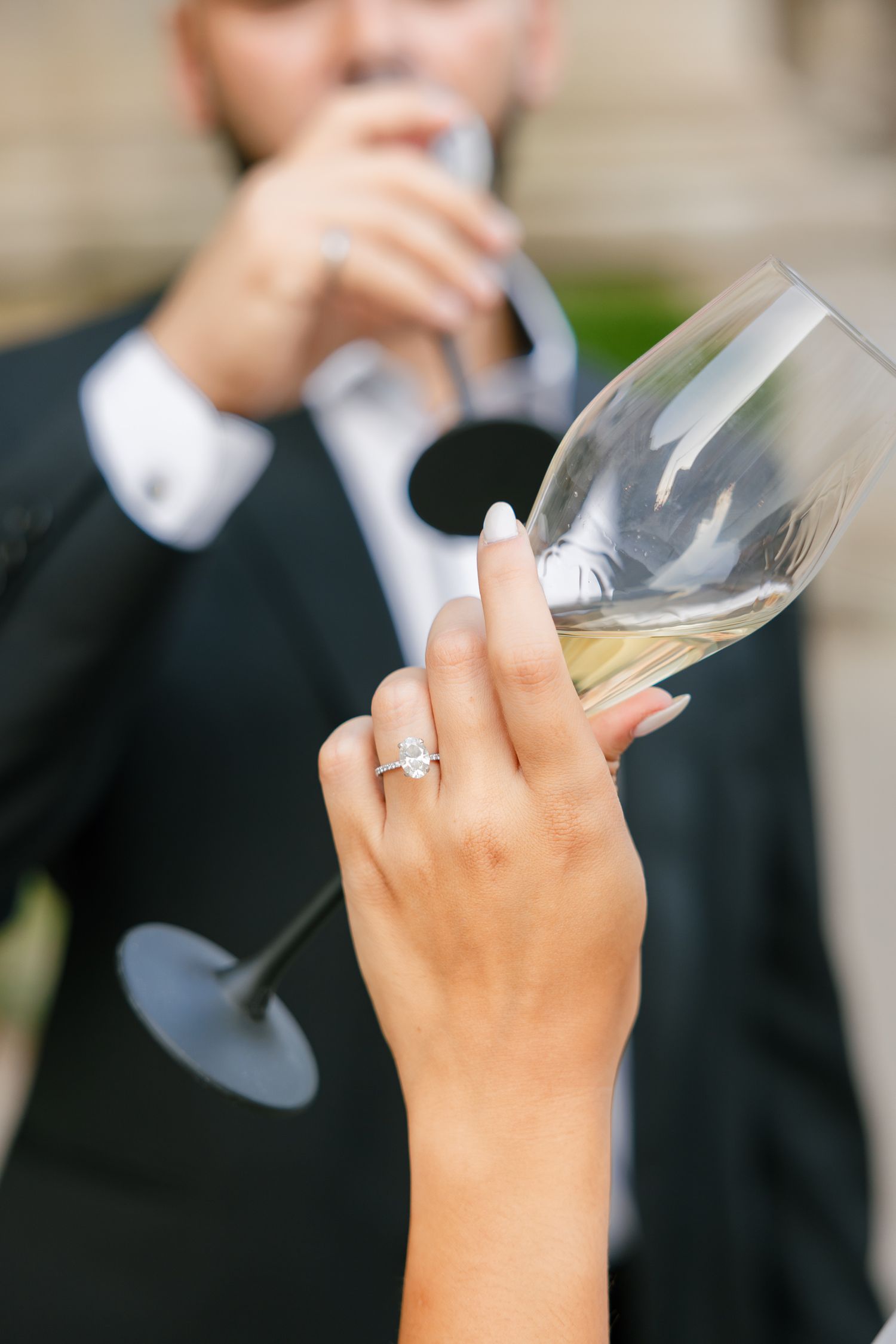 Close-up of hand with engagement ring holding wine glass during outdoor celebration.