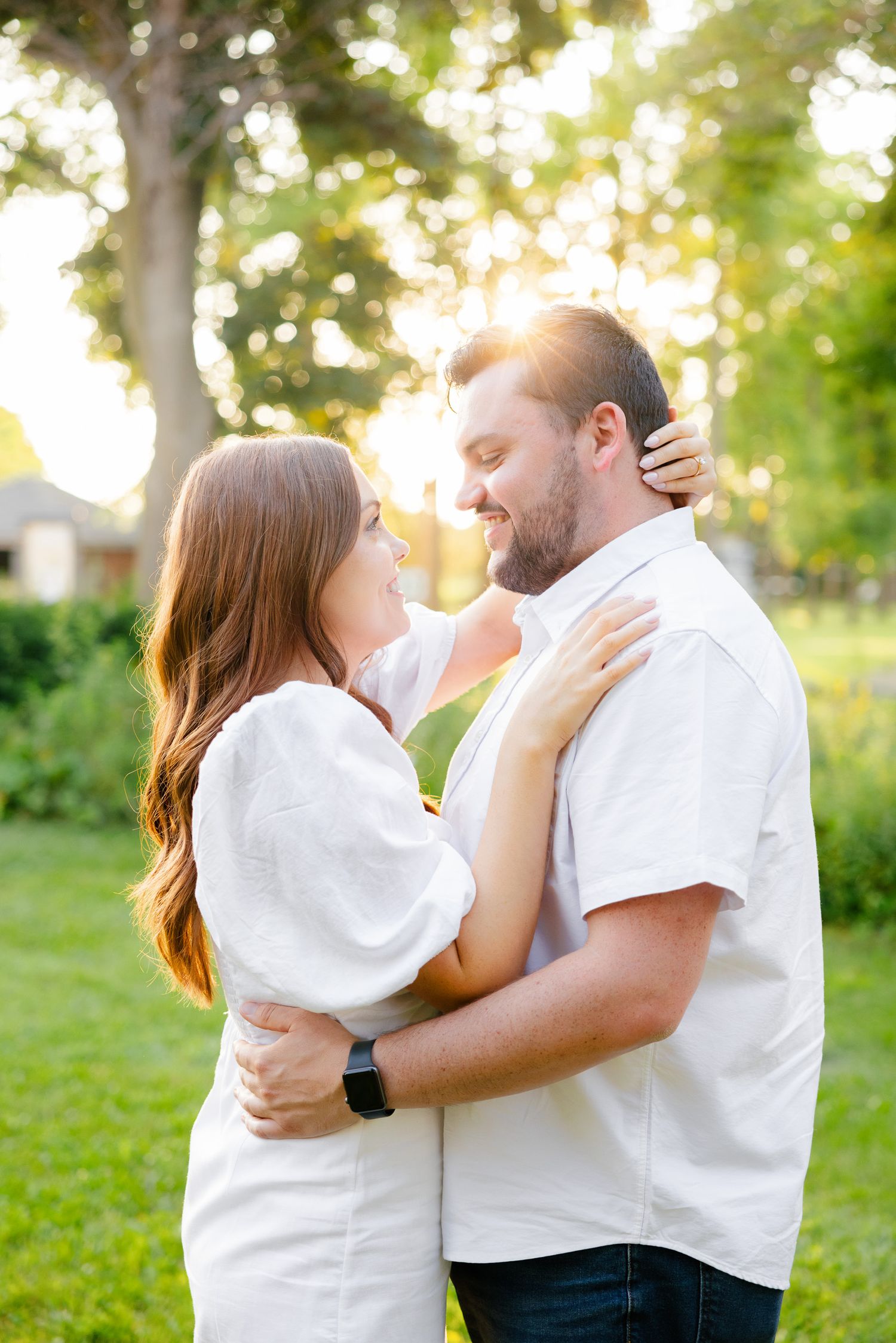 A tender embrace between a couple wearing white against a sunset-lit garden background.