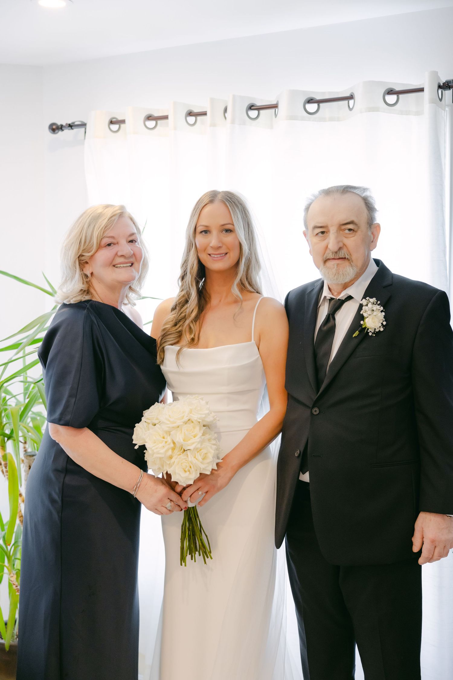 Wedding portrait of three people in formal attire with white bouquet.