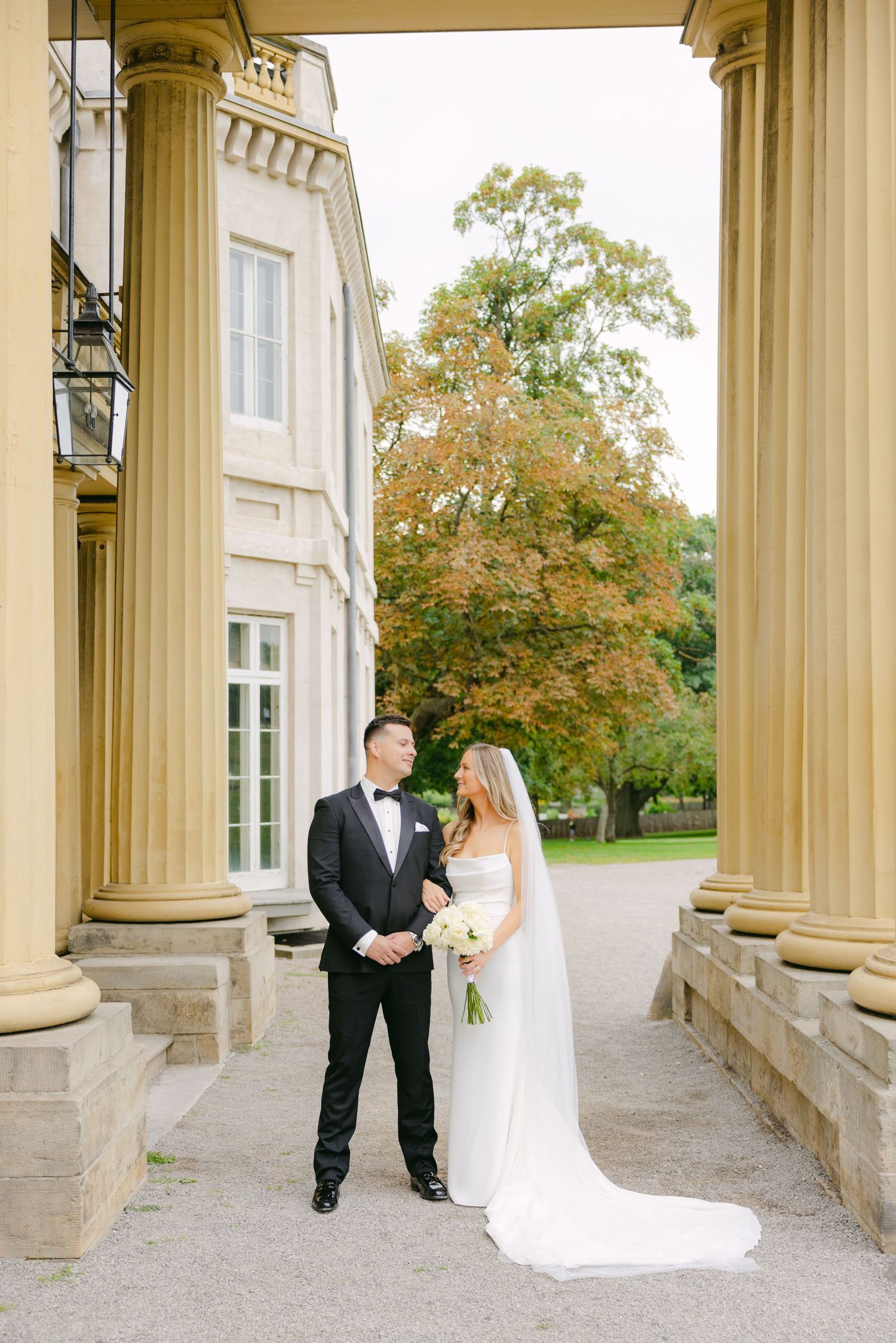 Elegant wedding photo framed by golden columns with autumn foliage in background.