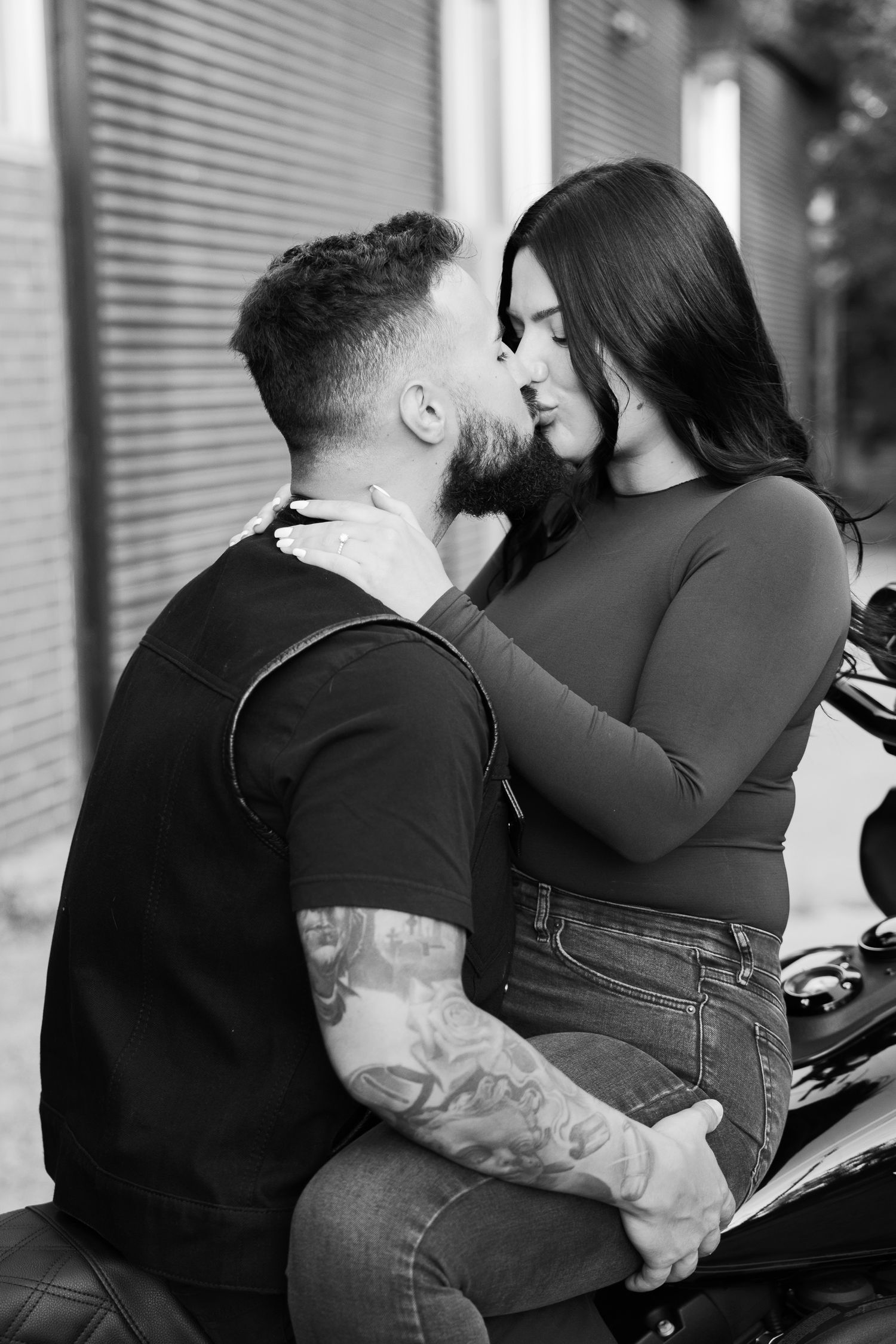 A couple embraces while seated on a motorcycle in a black and white portrait.