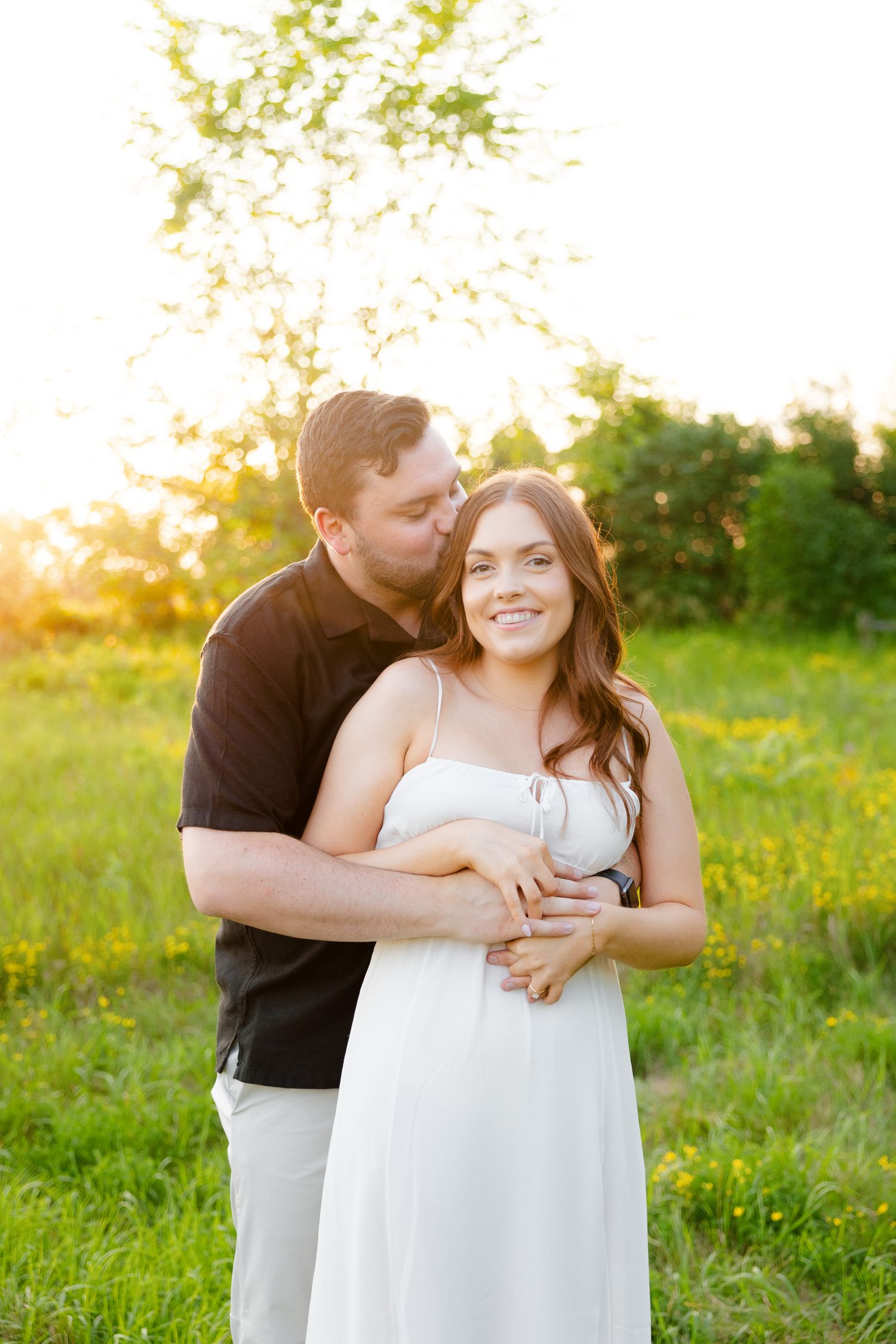 Romantic couple shares an intimate embrace in a sunlit field of wildflowers during sunset.
