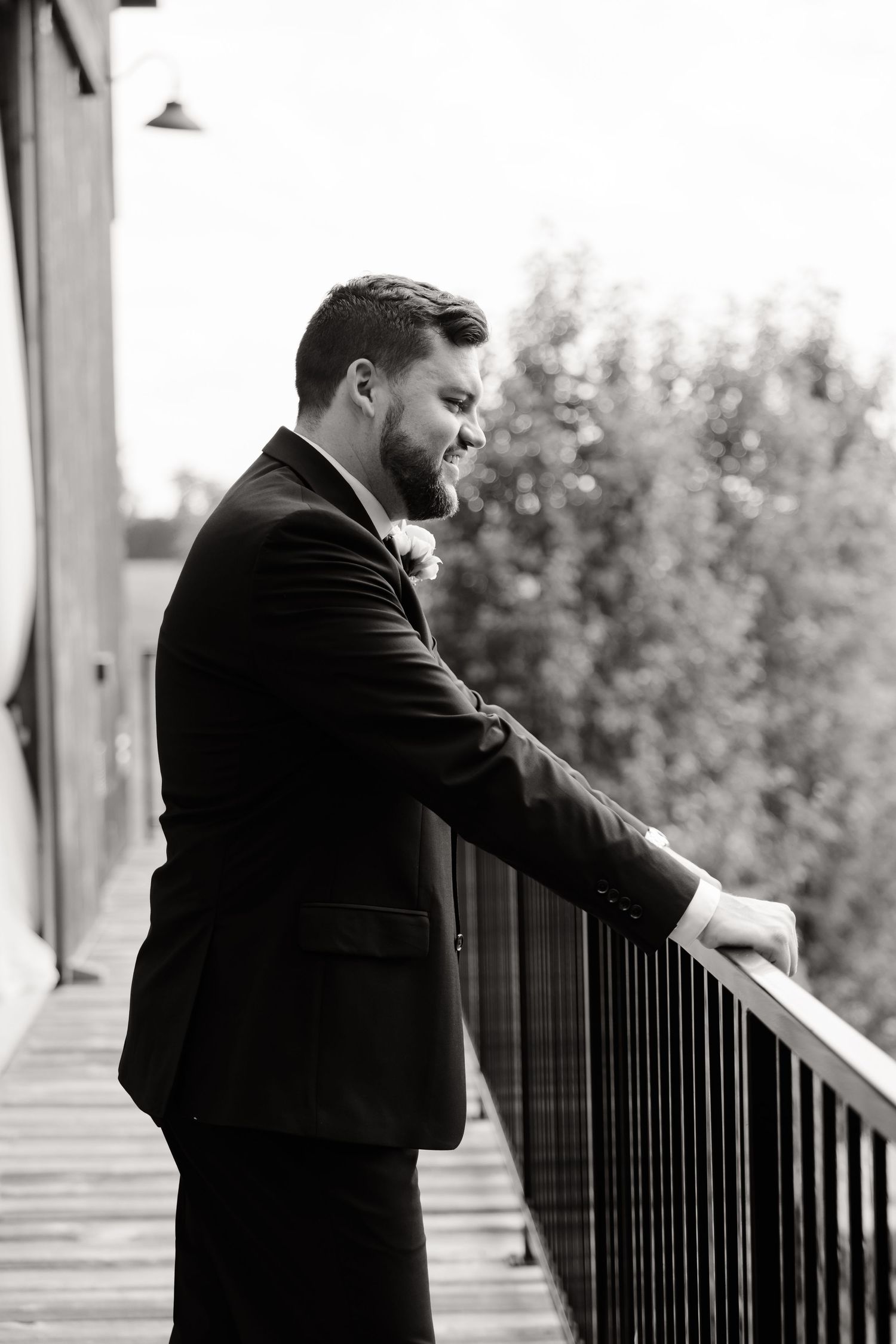 Black and white portrait of person in suit looking over outdoor balcony railing.