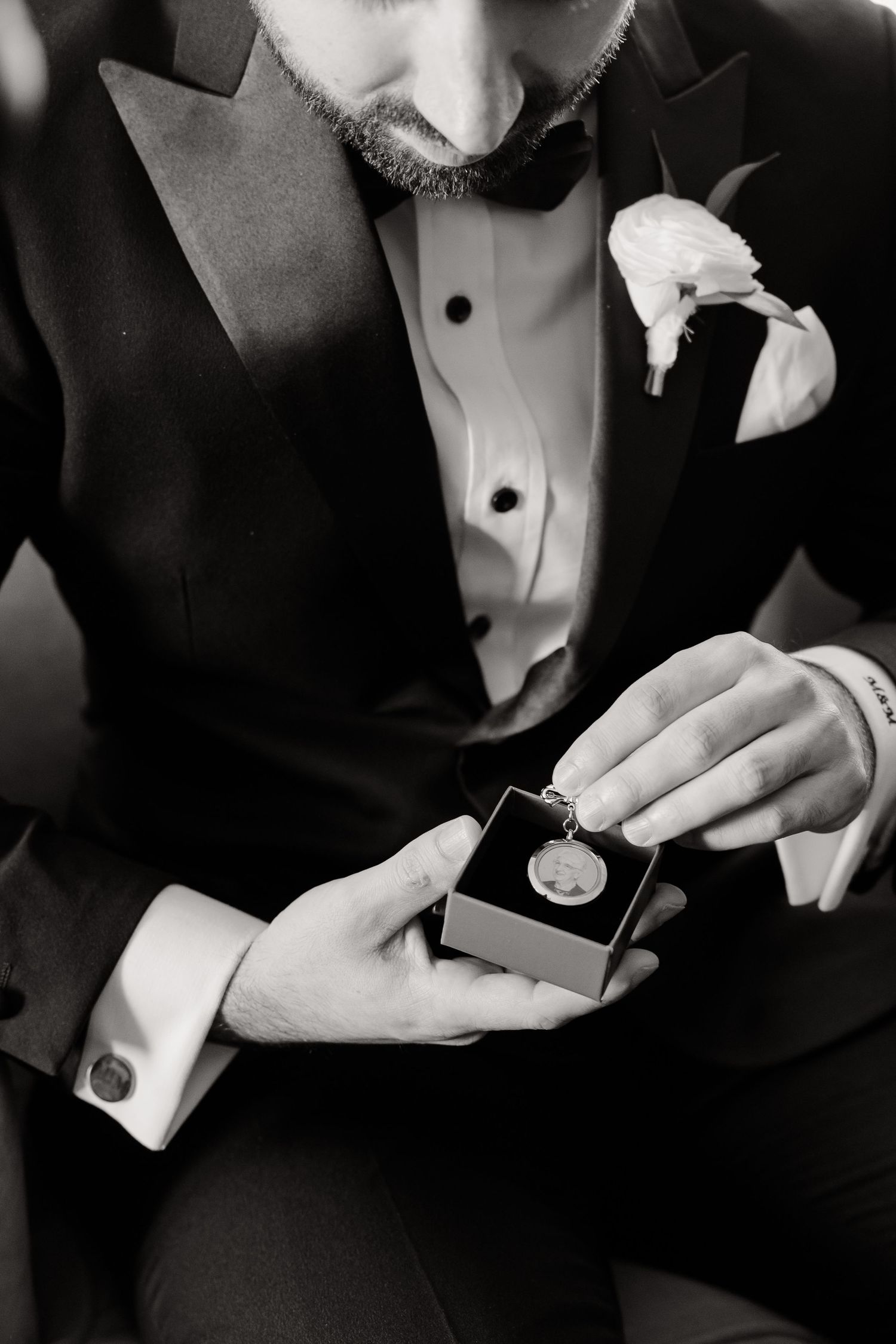 Close-up black and white shot of hands holding a small box with formal attire visible.