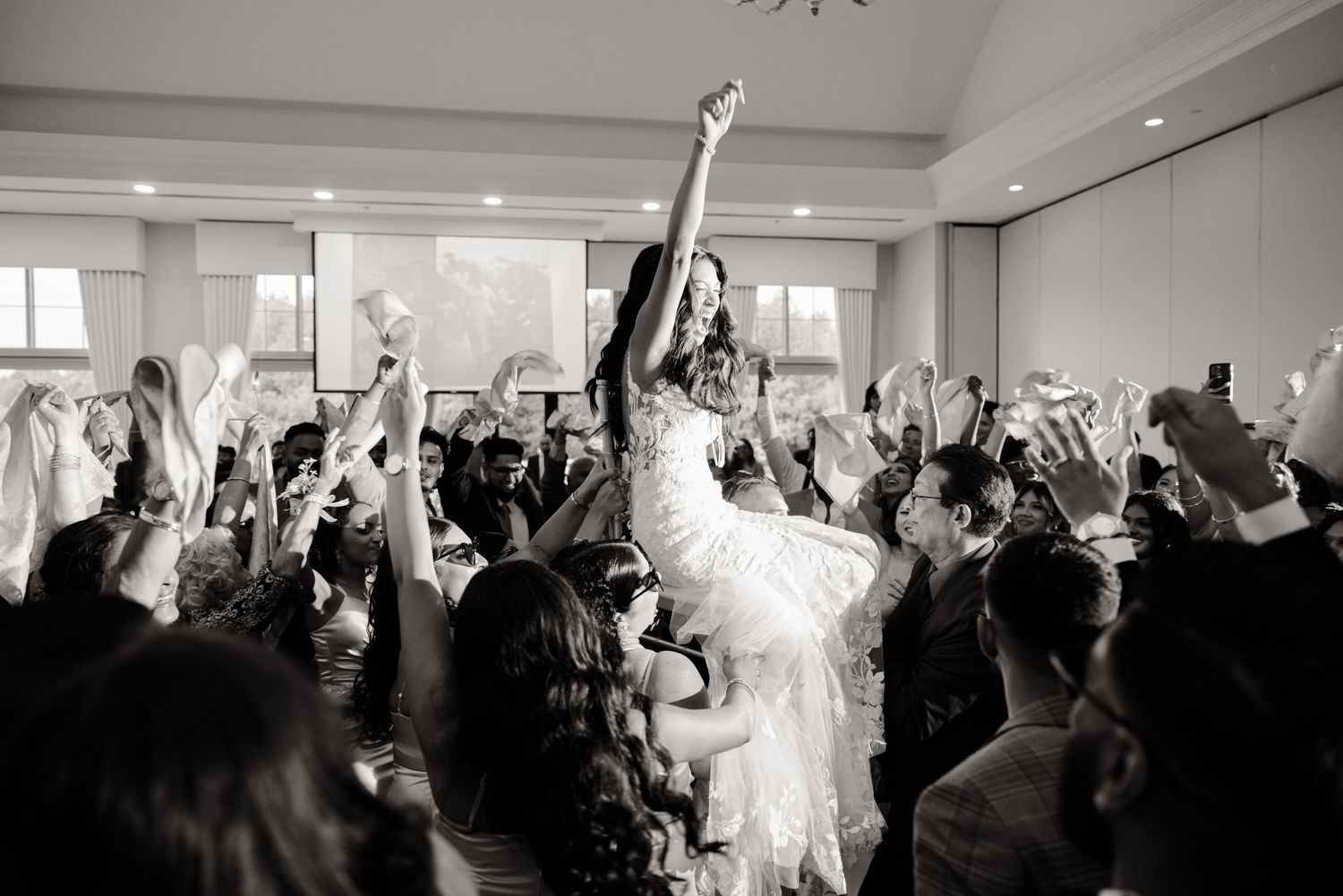 Wedding party celebrates with arms raised on the dance floor of an elegant reception venue.