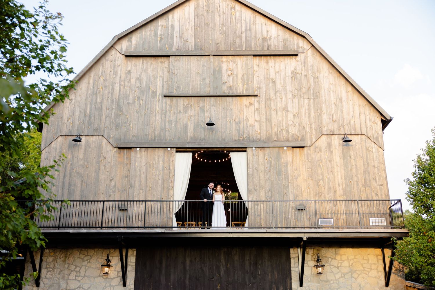 Wedding portrait taken at a weathered wooden barn featuring a dramatic balcony entrance.