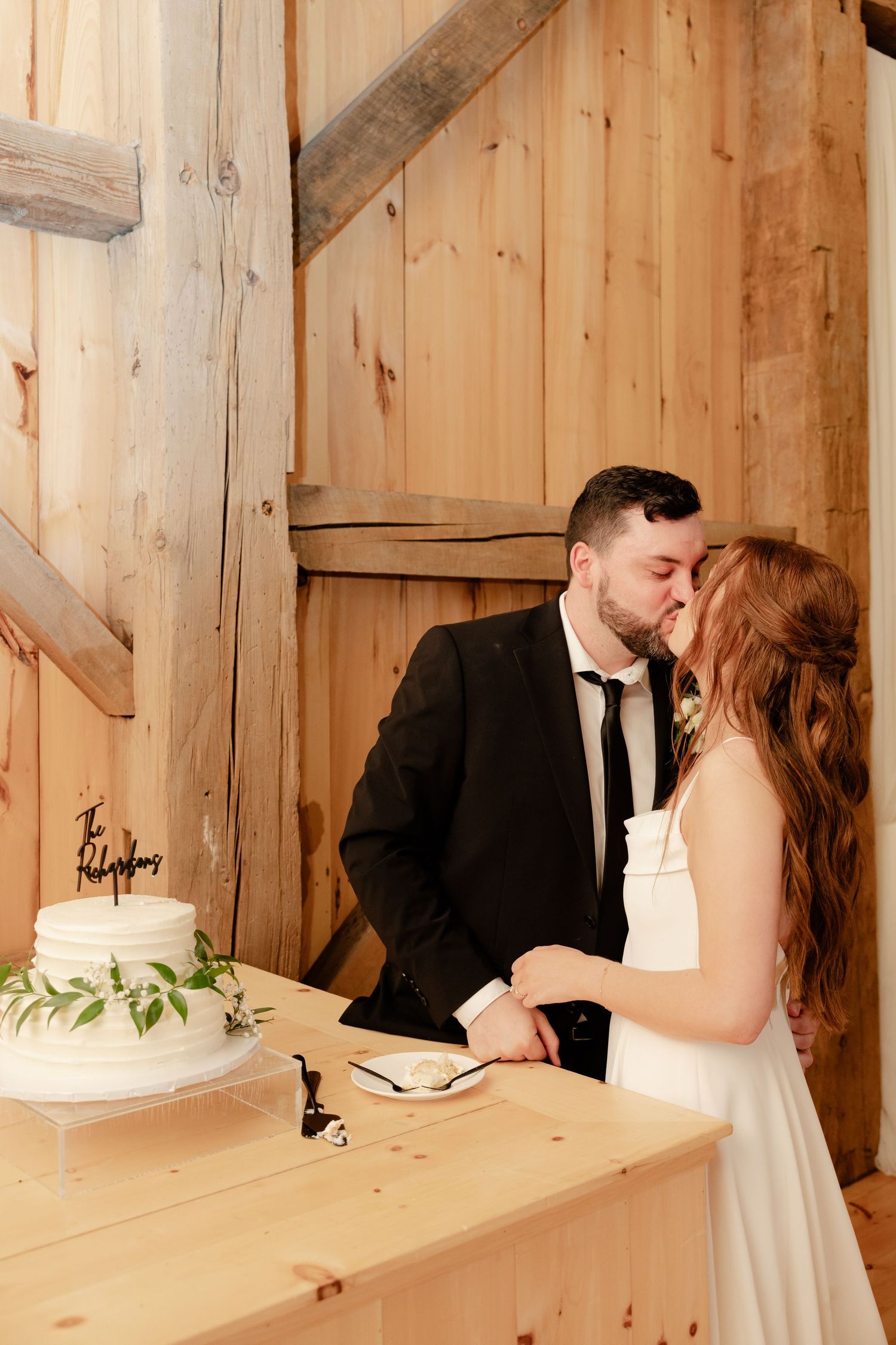 A romantic moment shared between newlyweds next to their wedding cake in a rustic barn venue.