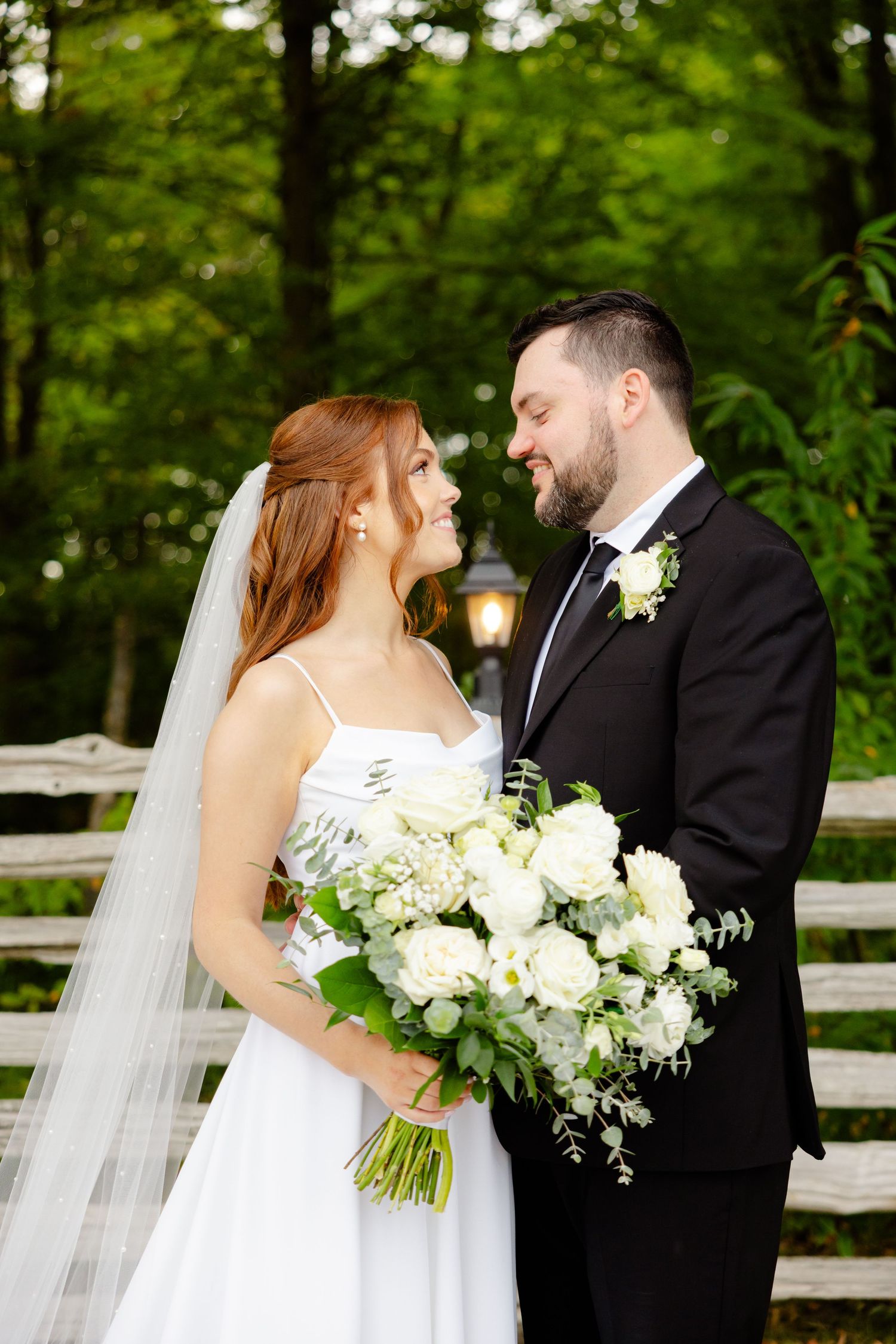 A romantic wedding portrait with the couple gazing at each other in front of a rustic fence.