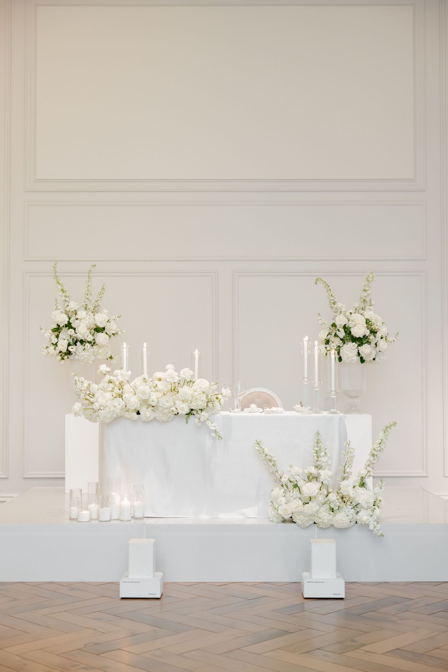 All-white wedding head table decorated with candles and cascading floral arrangements.