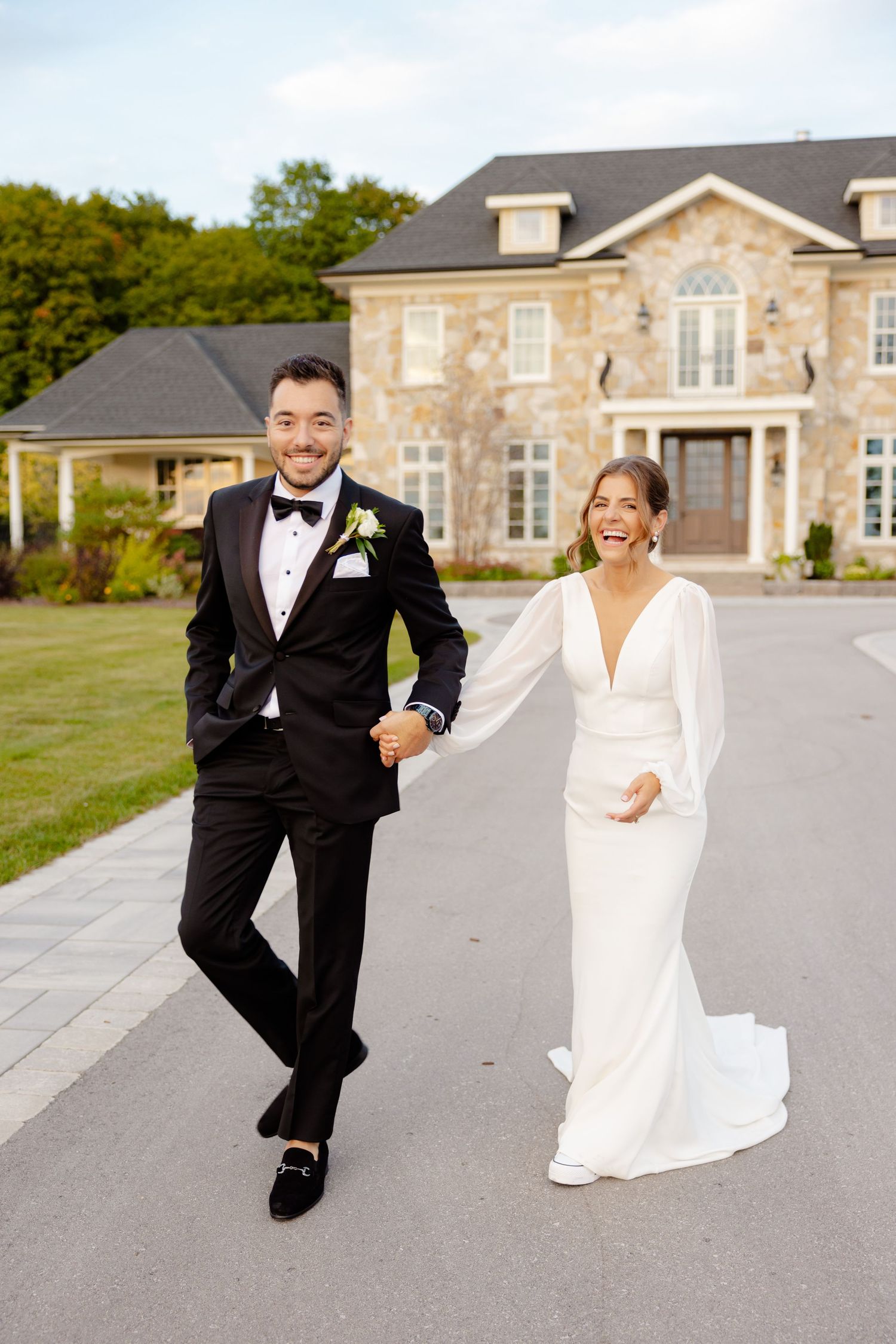 A joyful couple laughing together outside a beautiful stone house on their wedding day.