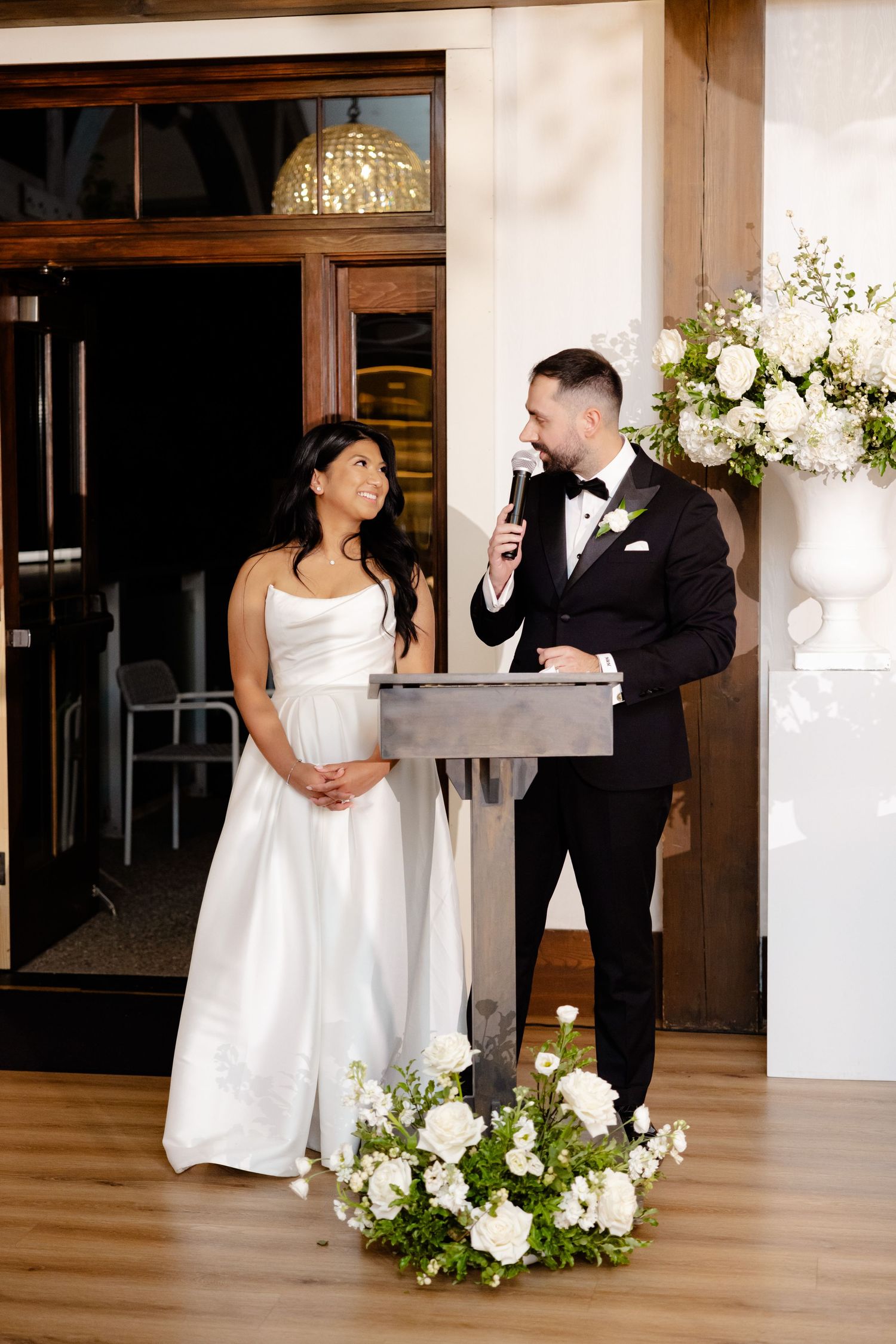 Wedding reception speech at podium decorated with white floral arrangements.