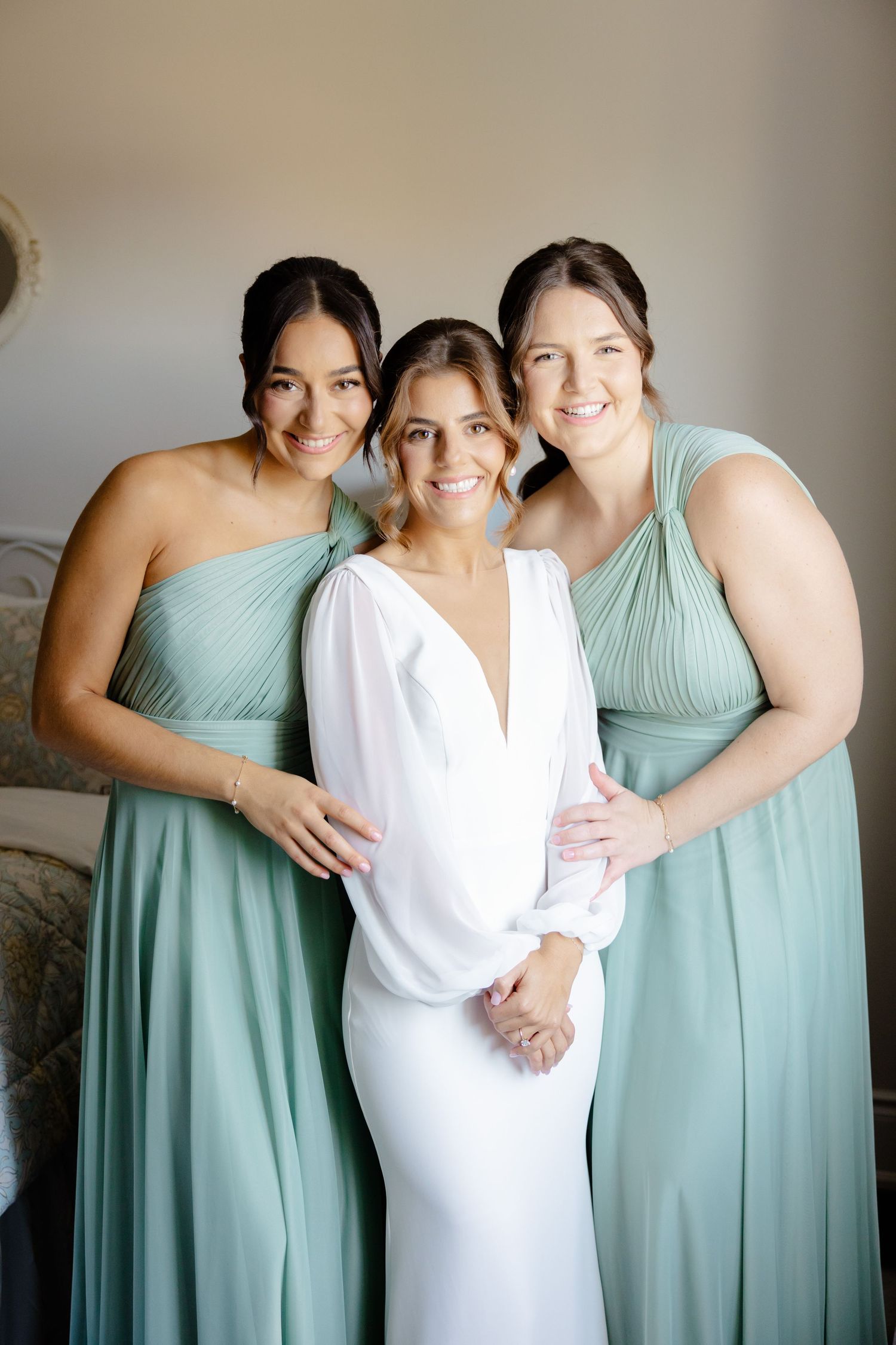 Bridesmaids in mint green dresses pose with a bride wearing an elegant white gown in a soft-lit room.