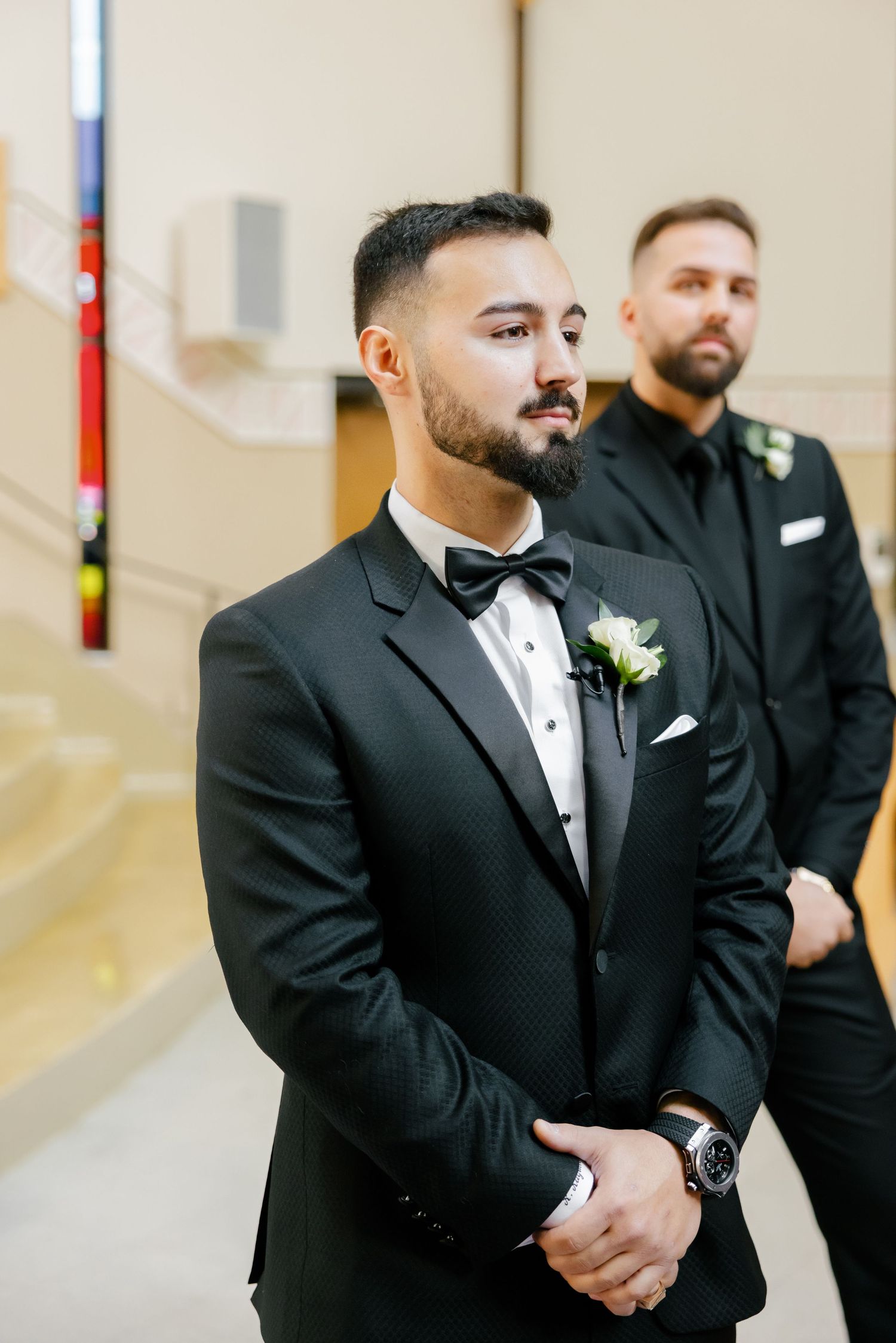 A groom in a black tuxedo and bowtie stands at attention during a wedding ceremony.