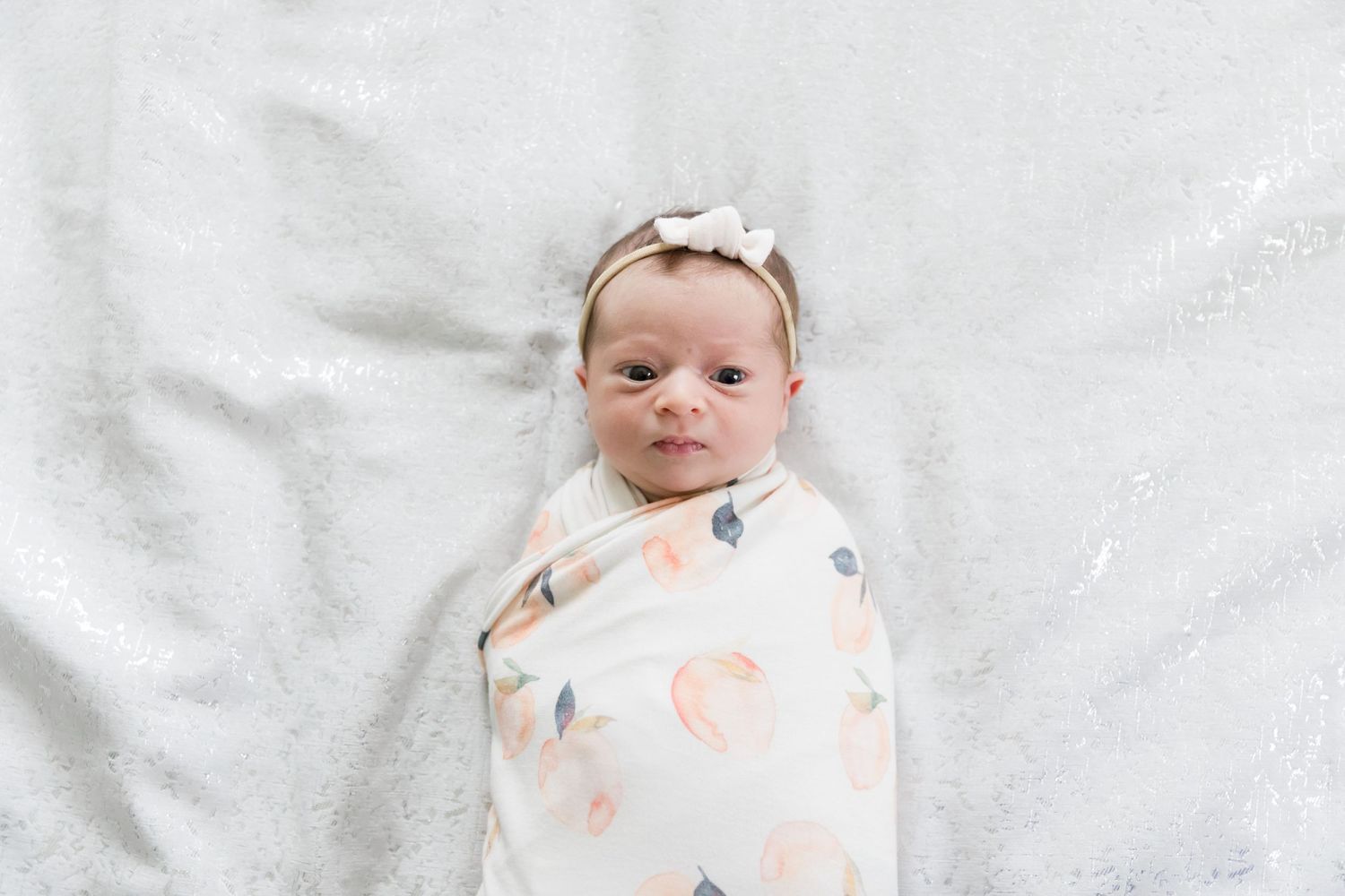 Newborn baby swaddled in floral print blanket smiling on white background.