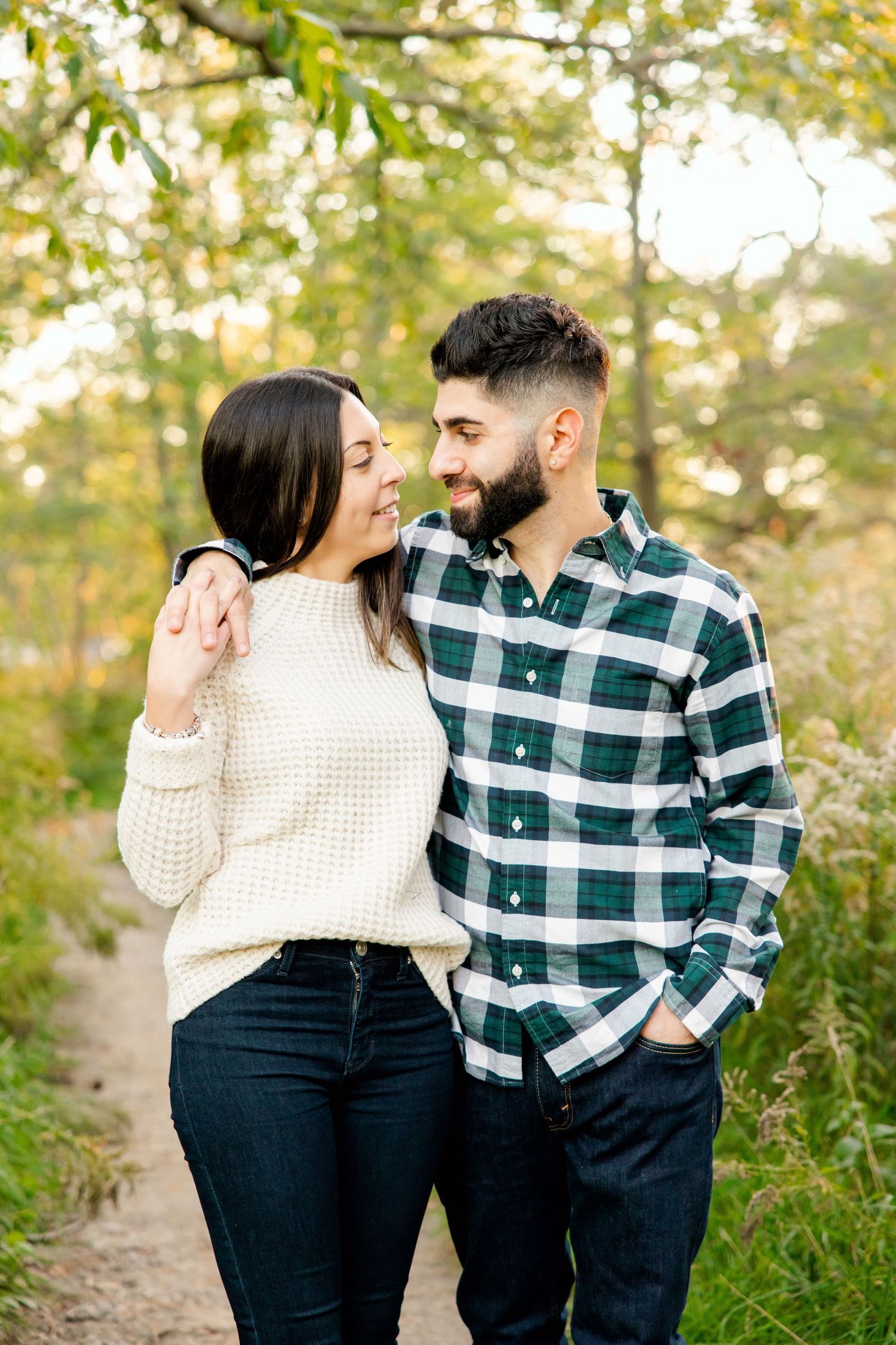 Intimate moment between couple in coordinating sweater and plaid shirt on forest path.