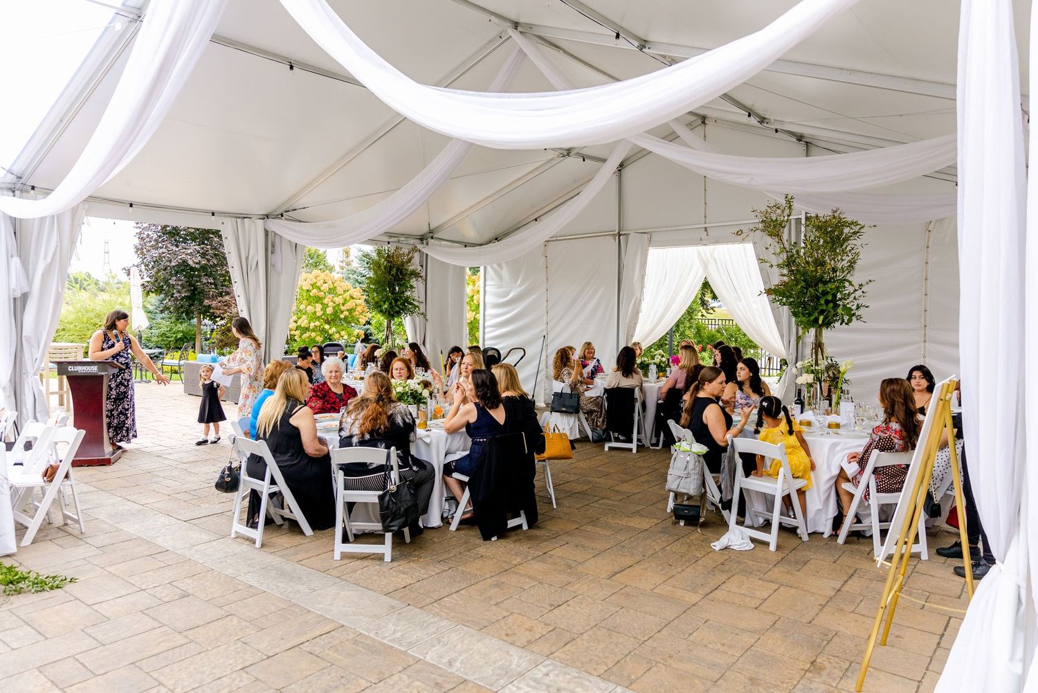 White tent venue filled with guests seated at round tables for a special celebration.