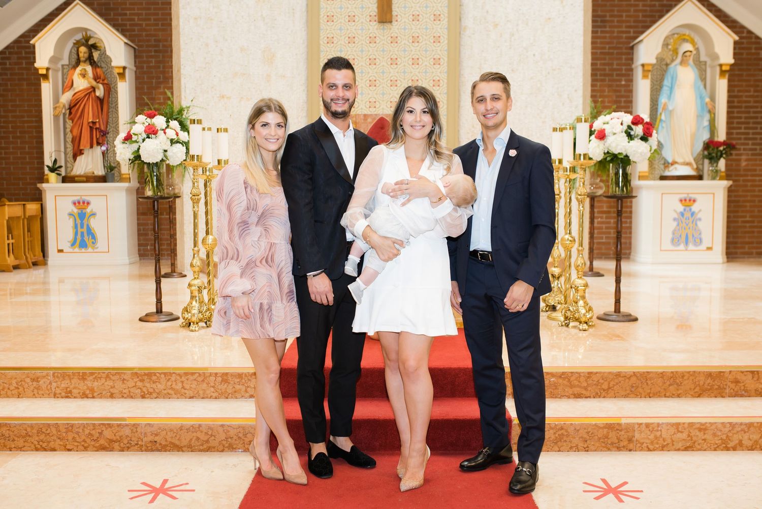 A baptism ceremony in a Catholic church with religious statues and white floral arrangements on display.