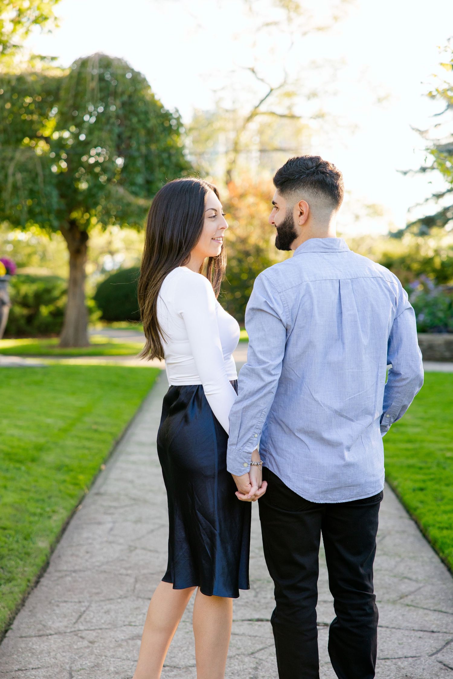 Couple holding hands while walking along a garden path surrounded by lush greenery.