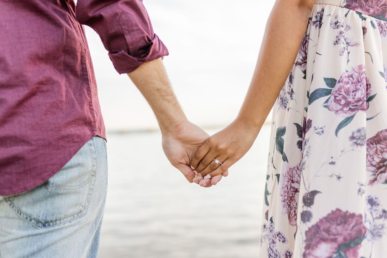Close-up of couple holding hands outdoors, wearing burgundy shirt and floral dress.