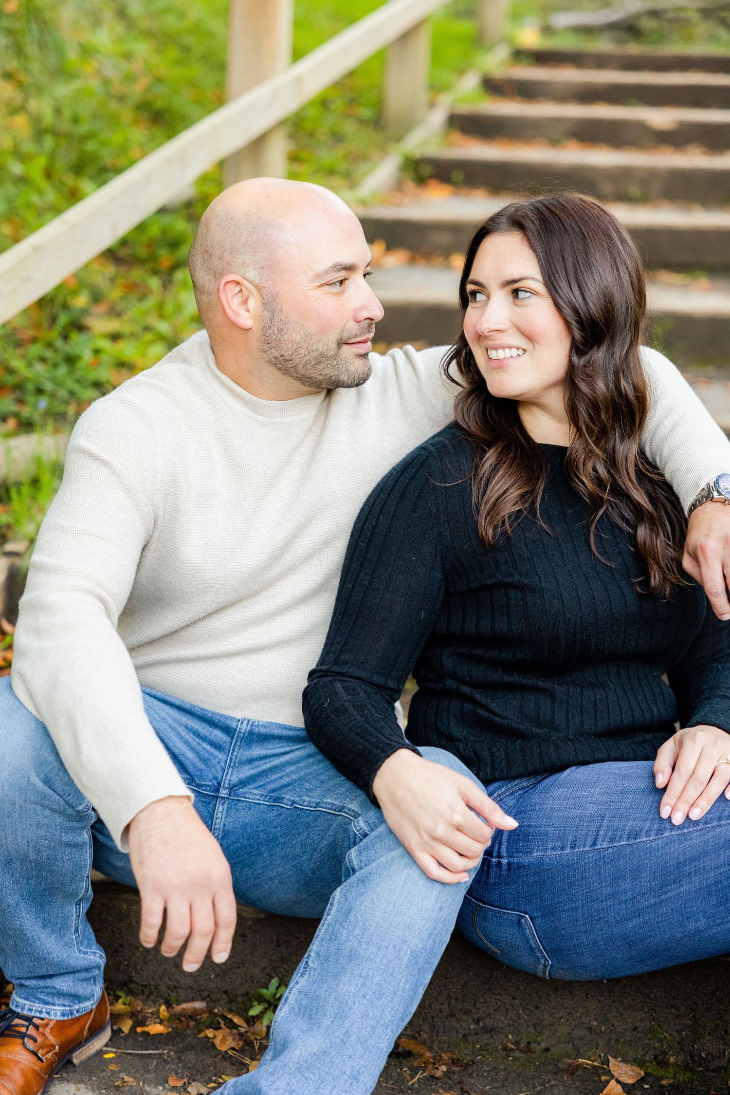 A couple gazes at each other while sitting close together on wooden stairs outdoors.