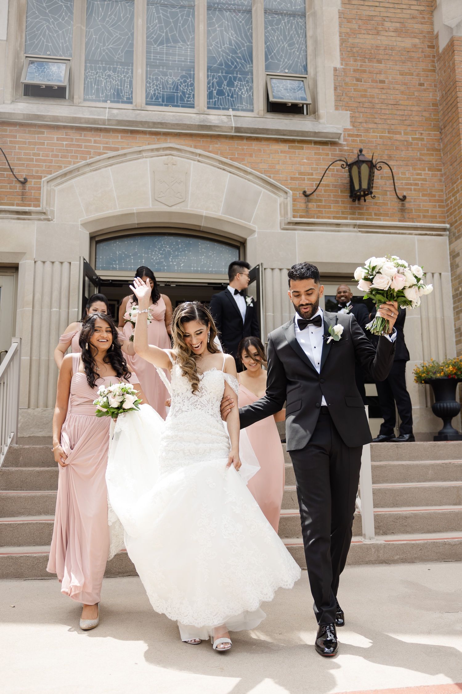 Wedding party descending church steps with bridesmaids in blush pink dresses.