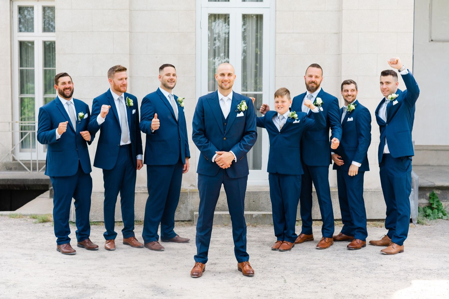 Groomsmen in navy suits strike playful poses outside classic building.