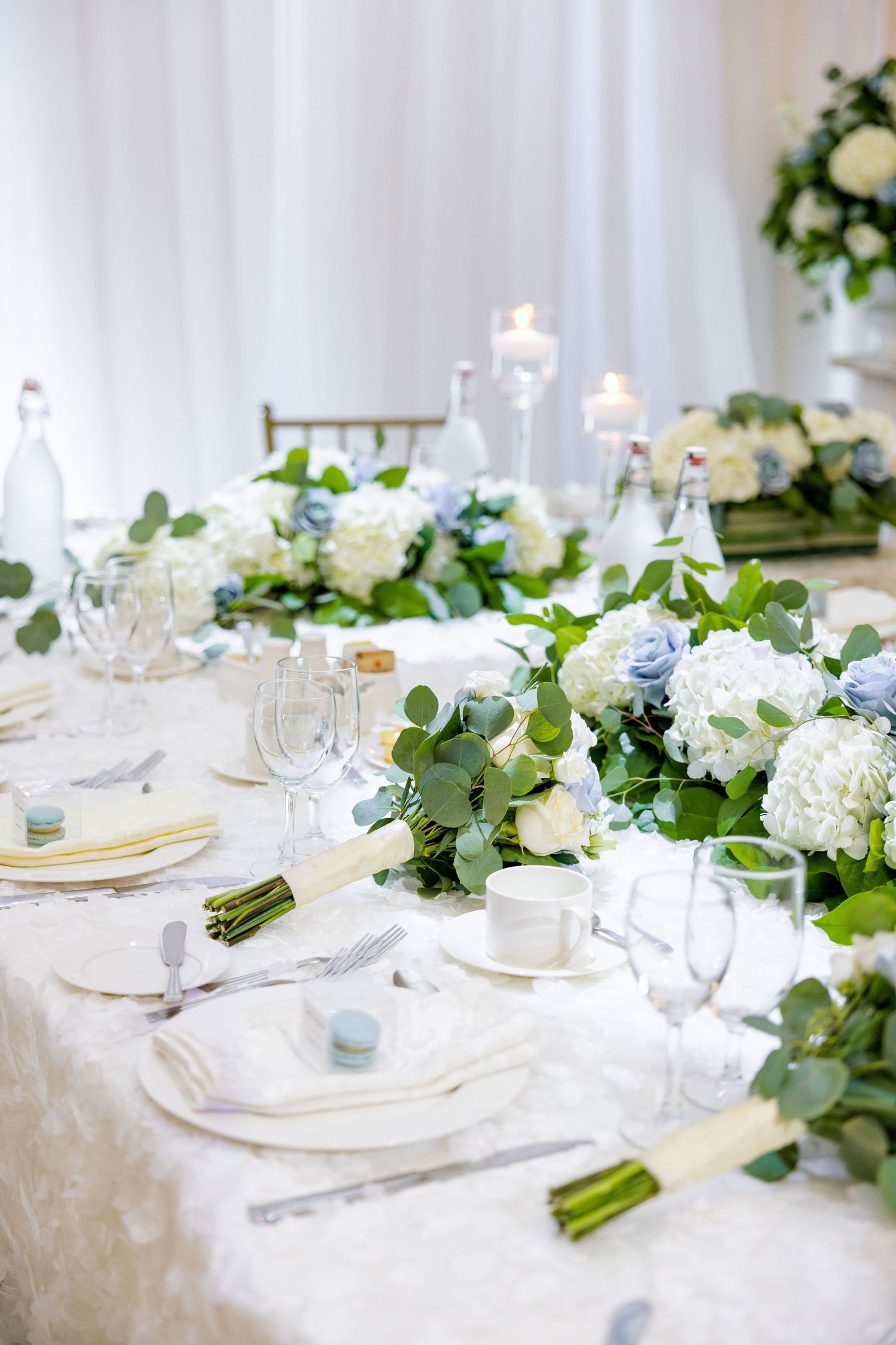 Elegant table setting with white and blue florals, glassware, and flowing greenery garland.