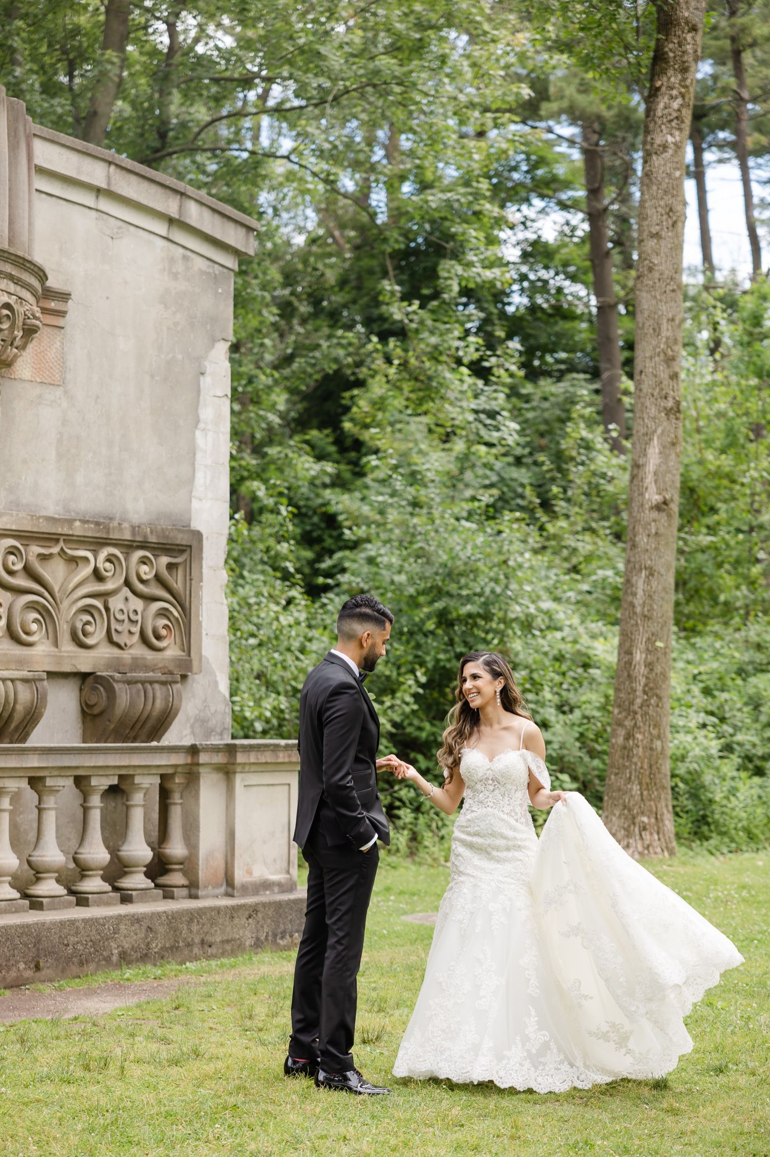 A wedding couple shares a moment near a decorative stone wall surrounded by greenery.