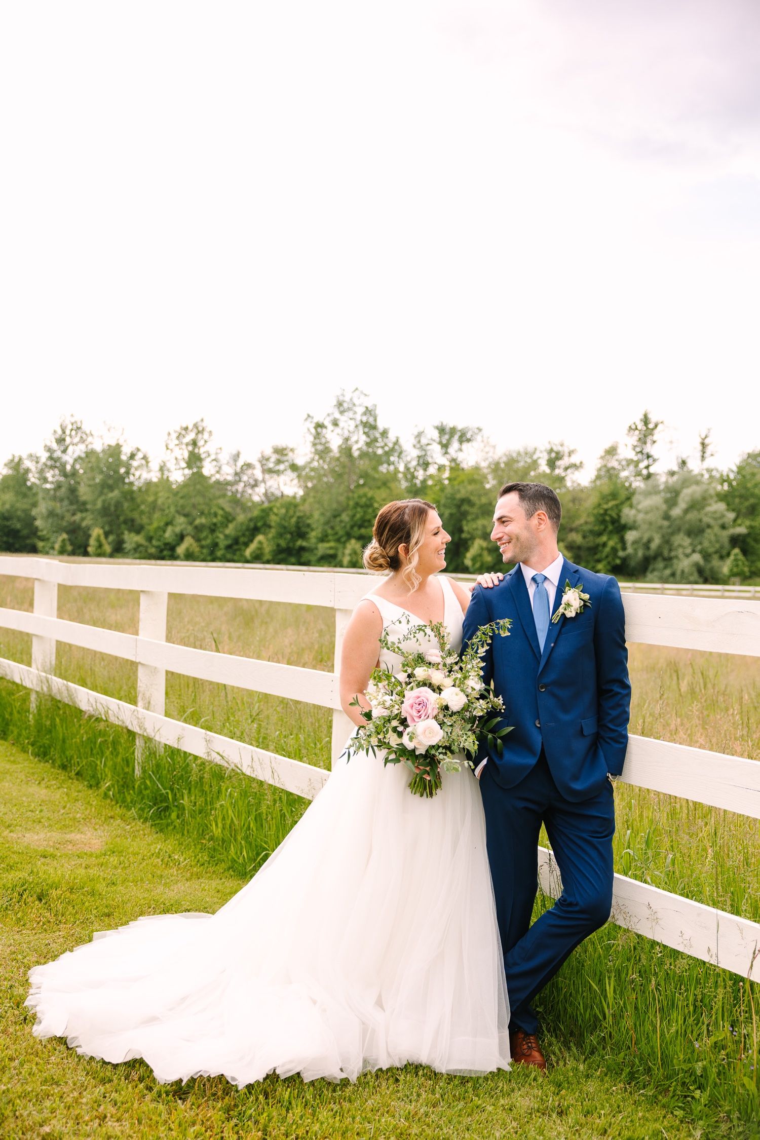 Countryside wedding portrait against white fence with soft lighting.