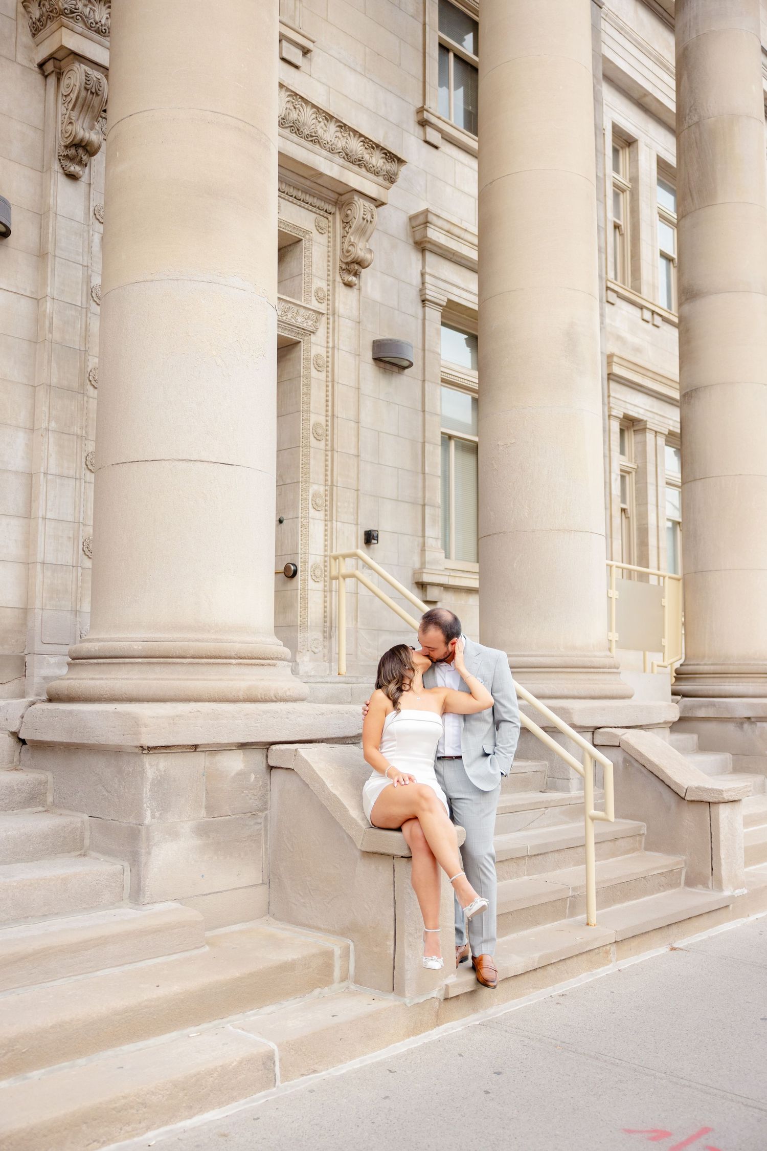 Elegant couple poses against classical architecture with large stone columns in background.