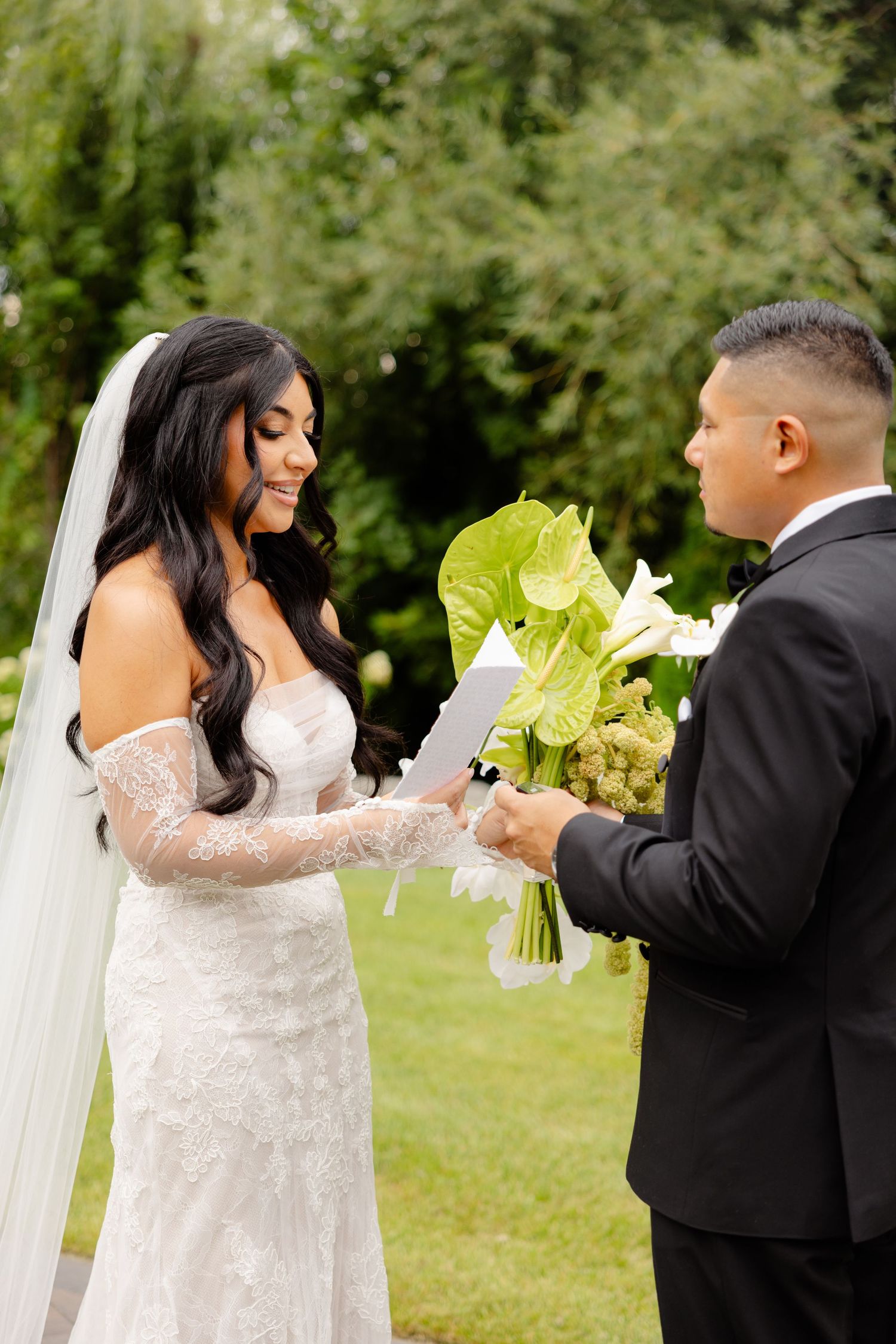 A couple exchanging vows outdoors during a wedding ceremony with lush greenery in the background.