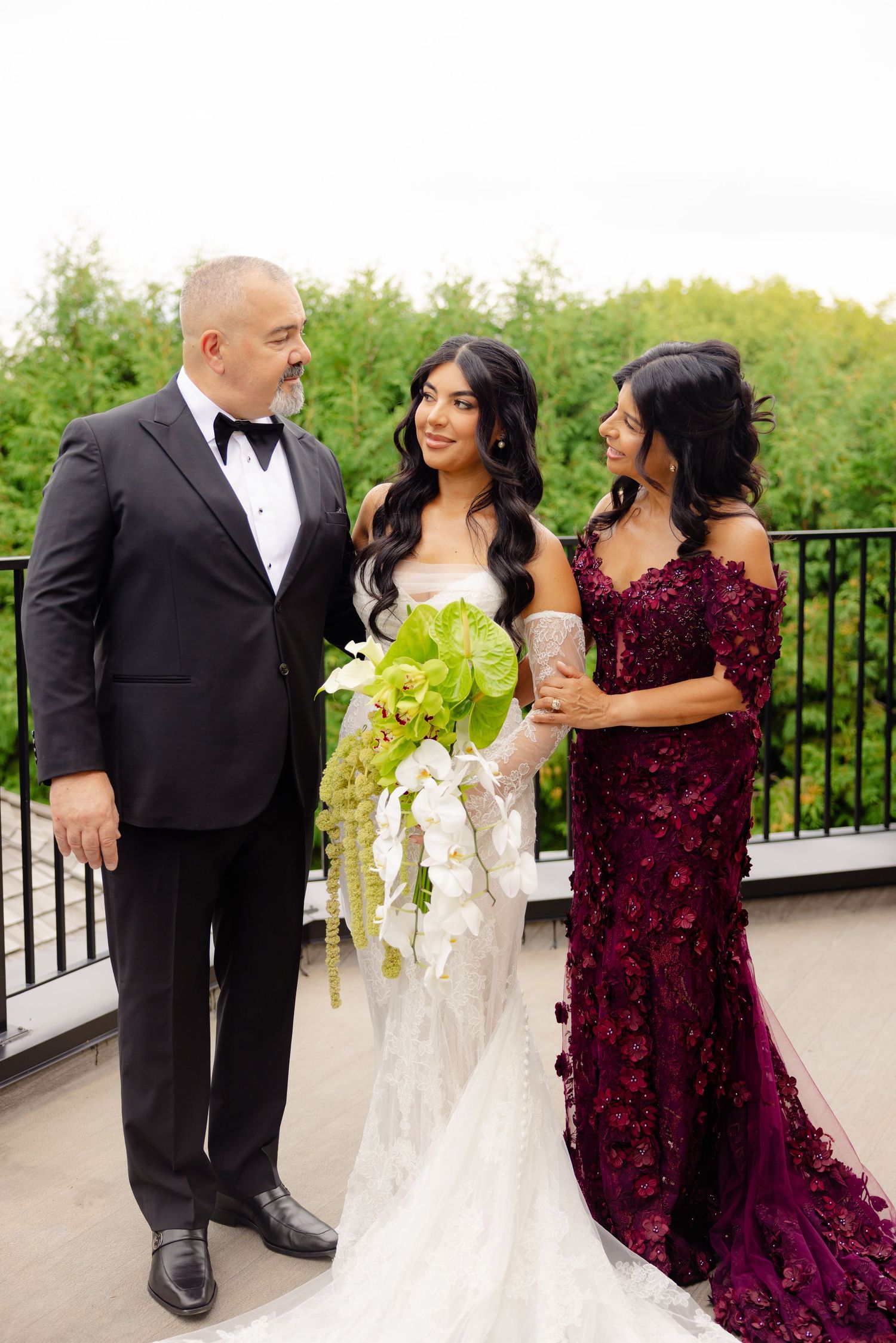A wedding party poses on an outdoor terrace with lush greenery, featuring a bride in white and guests in formal attire.