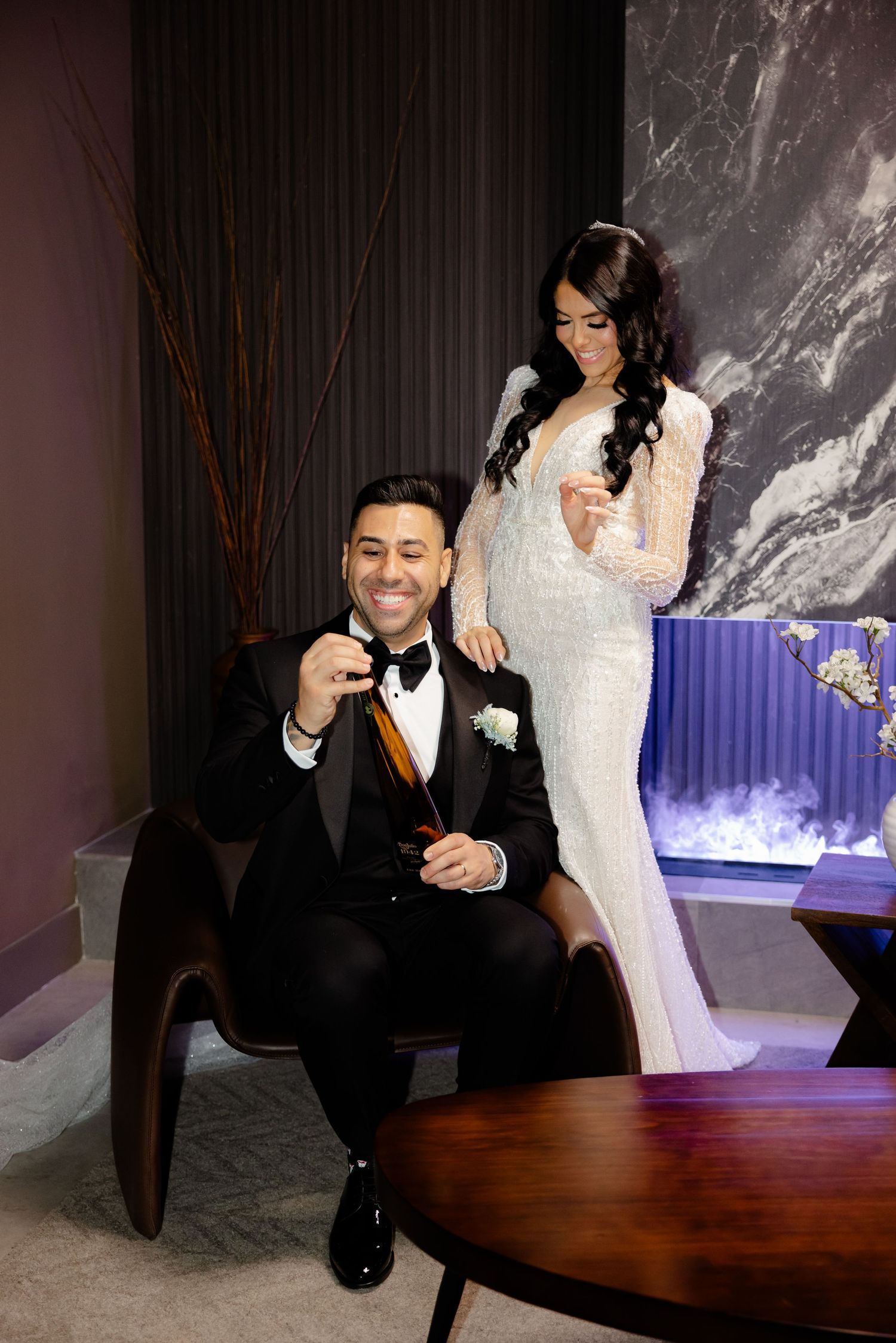 Elegant couple poses for wedding photos in a modern setting with marble walls and mood lighting.